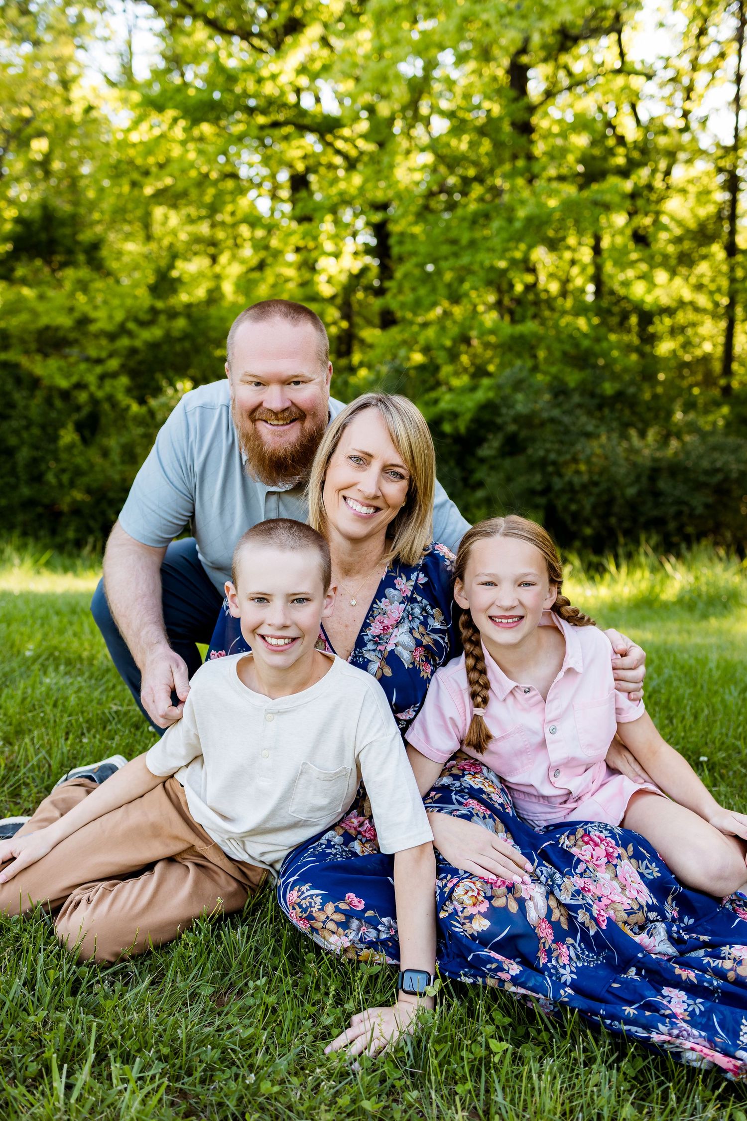Happy family of four sitting together on grass during a sunny outdoor photo session.