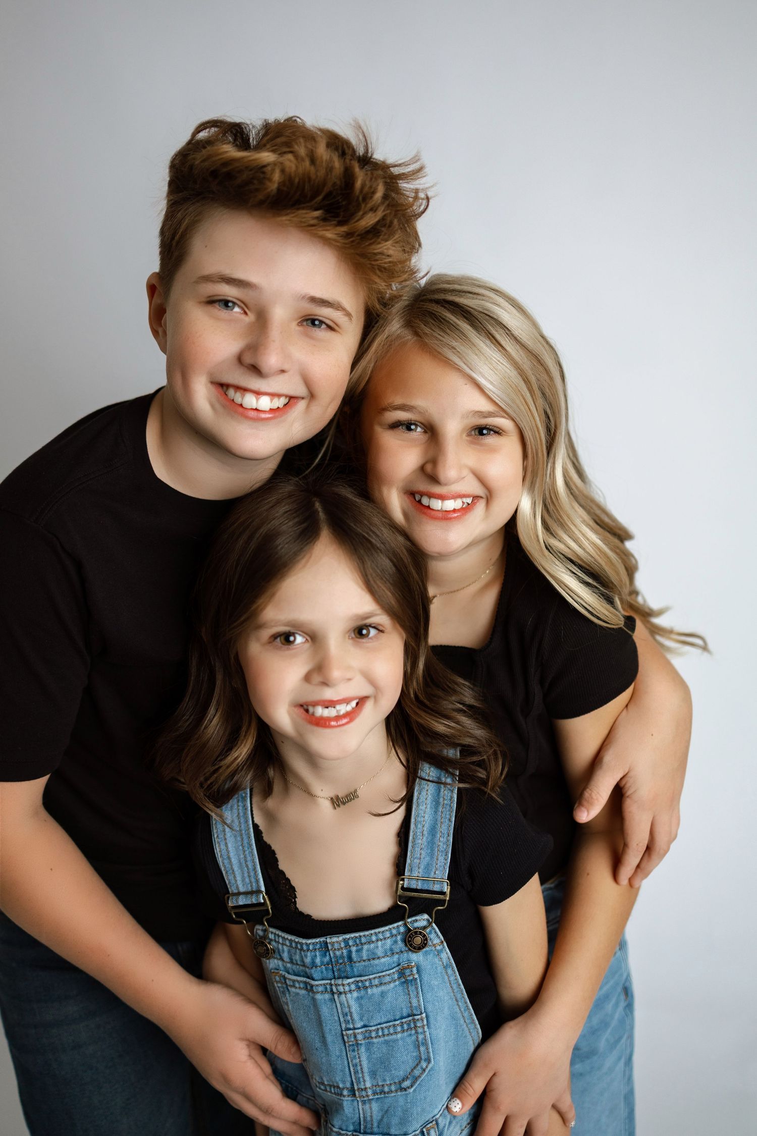 Three siblings pose together against a gray backdrop in a casual studio portrait series.