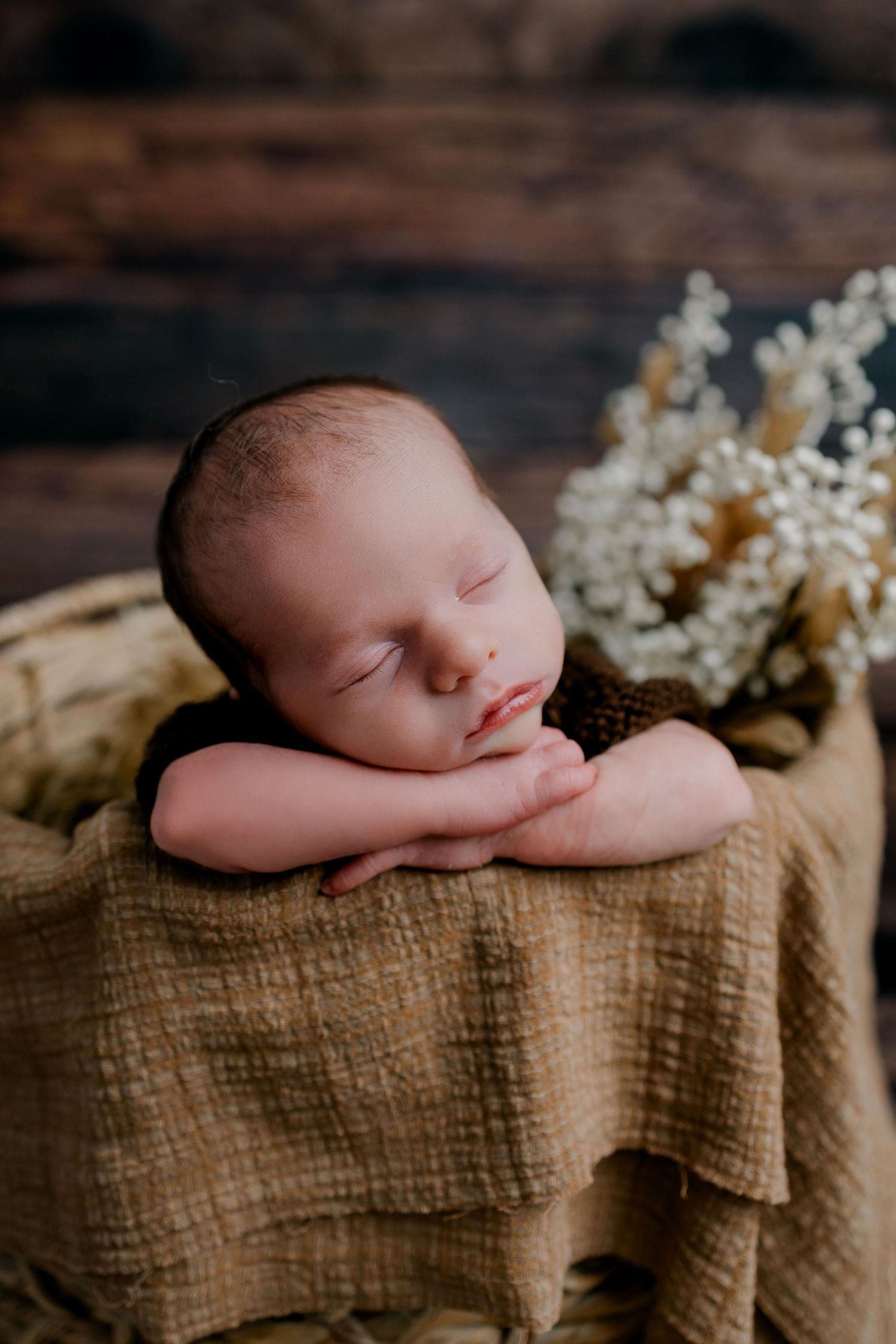 A sleeping newborn rests peacefully on textured burlap fabric with delicate white flowers in the backdrop.