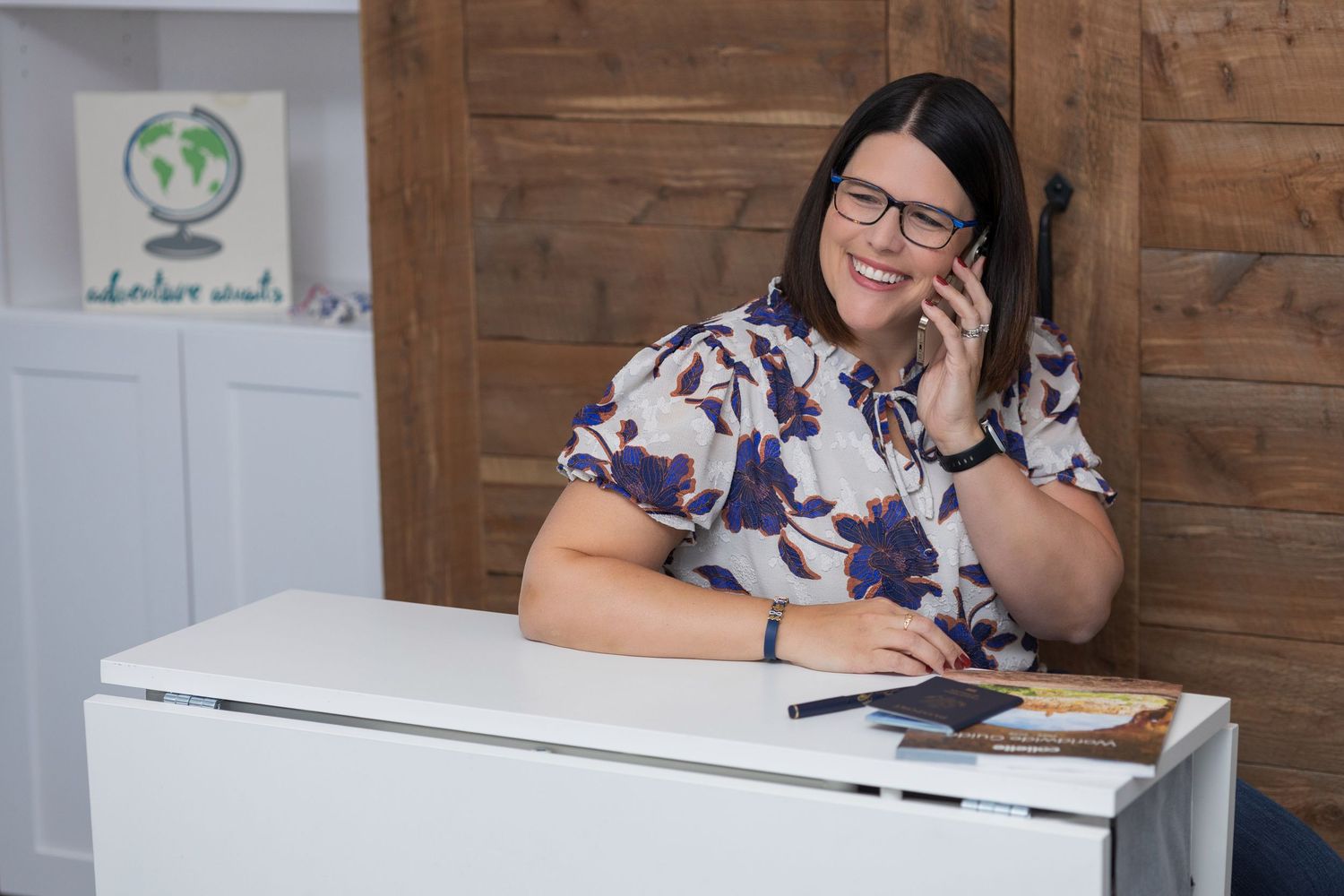 Person wearing glasses sitting at a desk writing in a notebook while laughing at the camera.