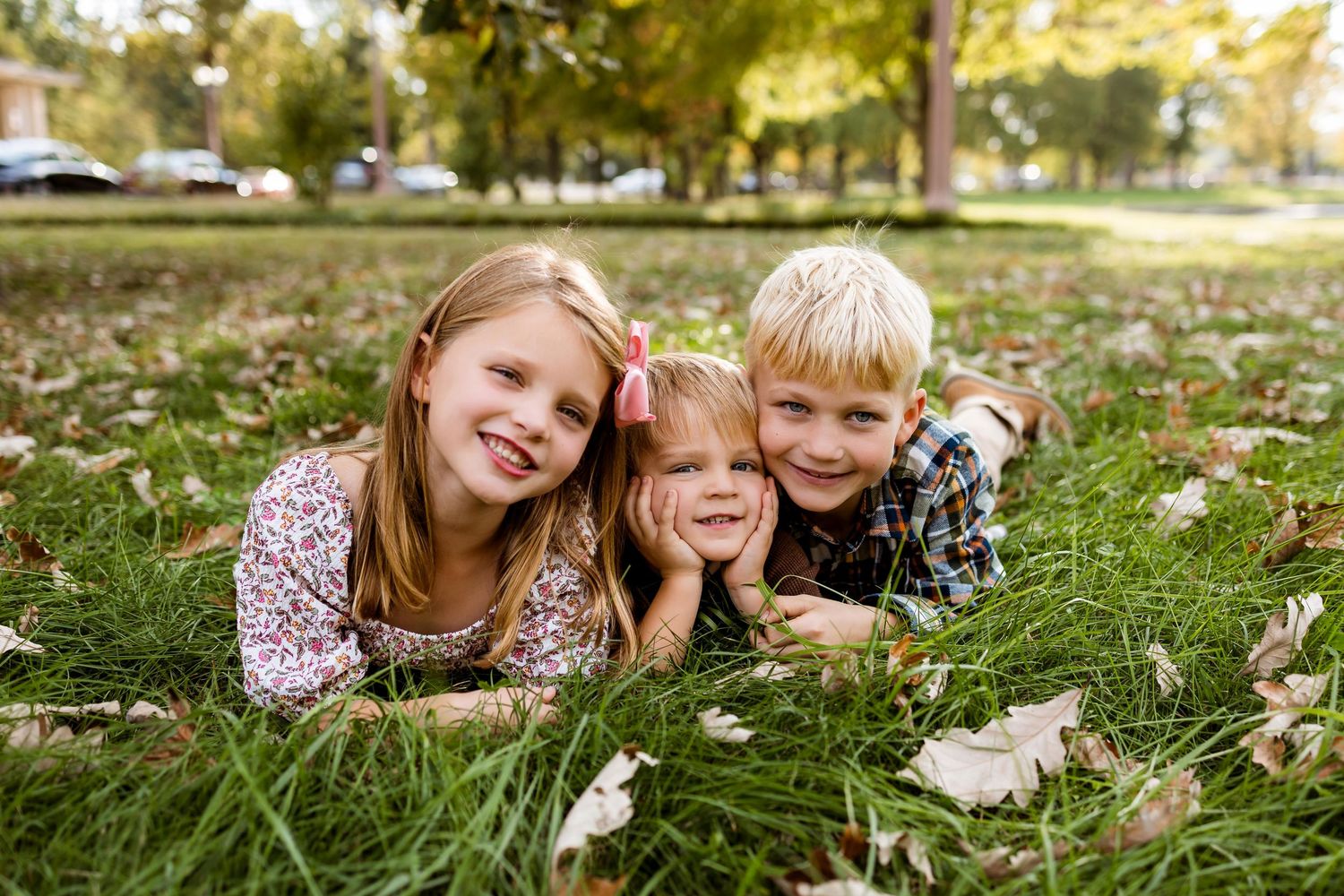 Family lying together on autumn grass during golden hour sunset in a park setting.