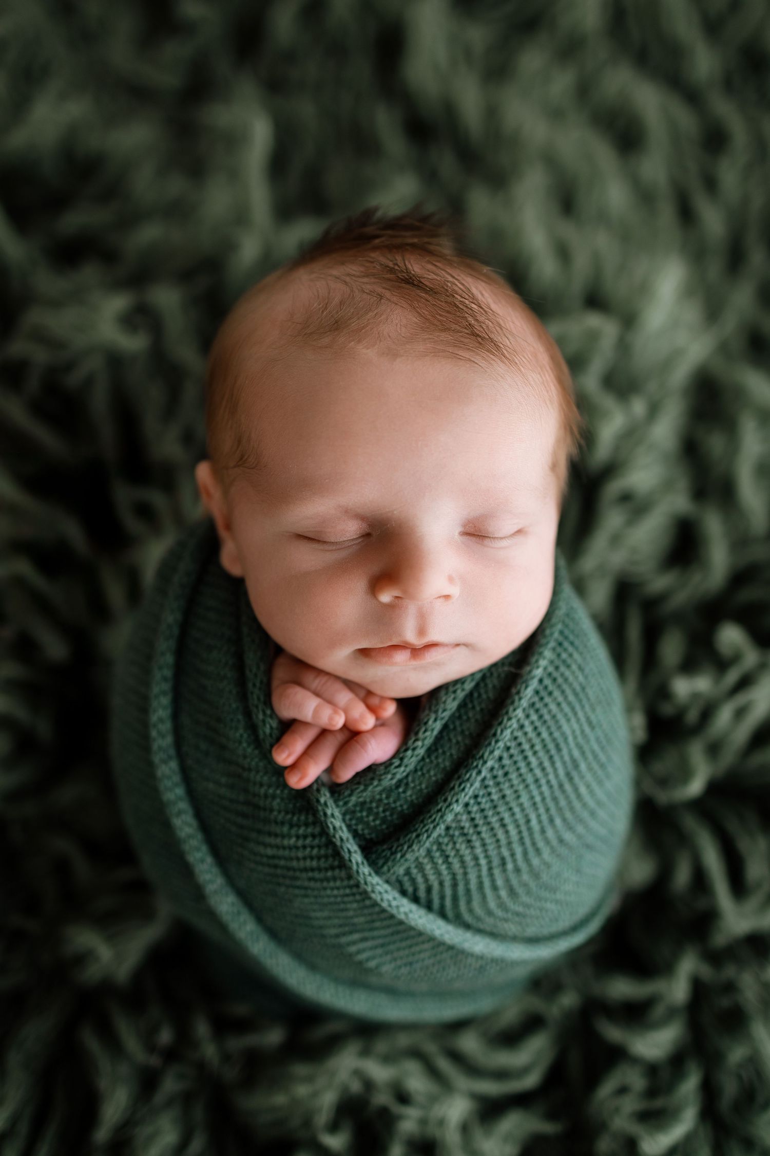 Sleeping newborn baby swaddled in a green wrap on a soft green fluffy blanket, peaceful newborn photography.