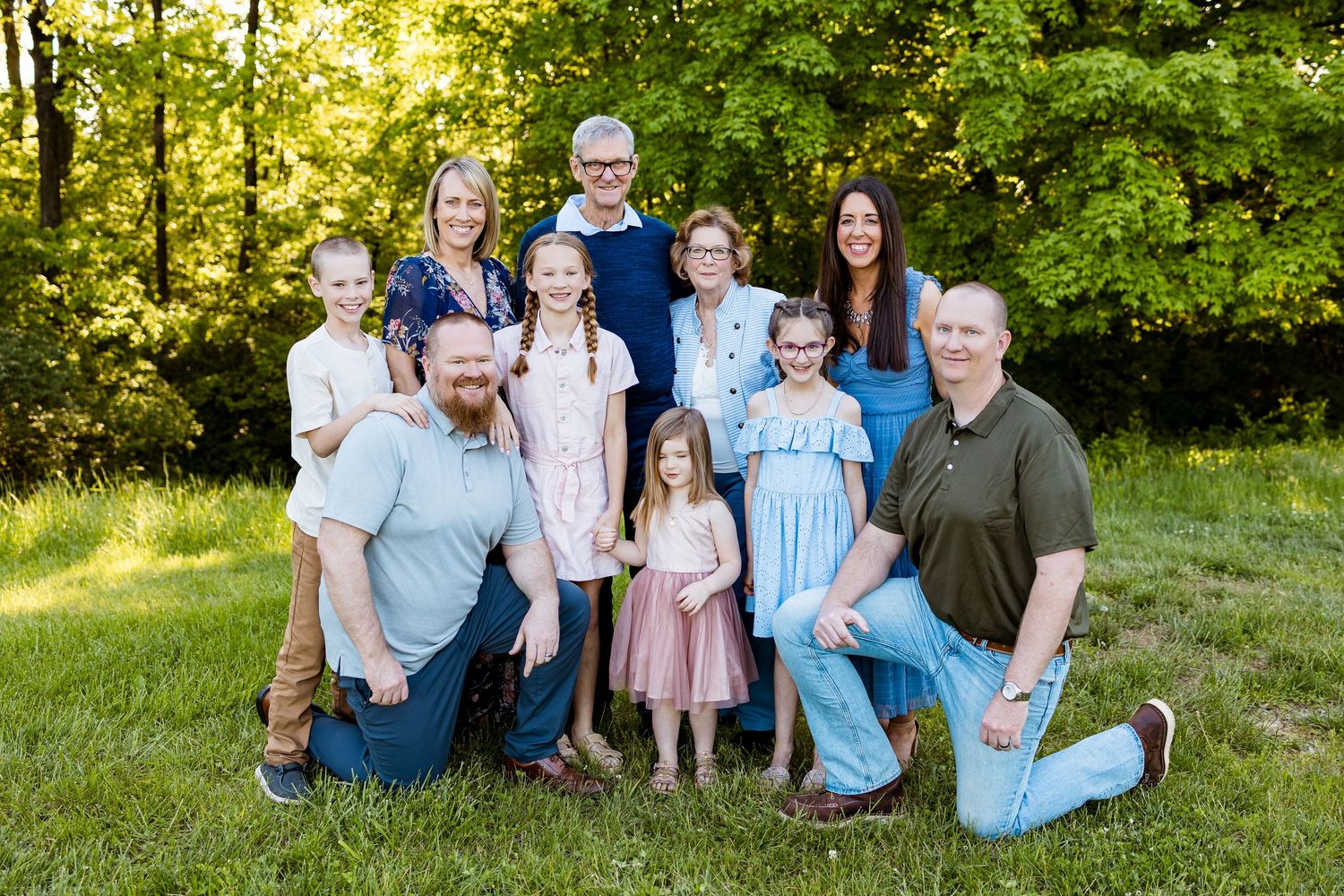 Multi-generational family group posed together in coordinated outfits against green foliage.