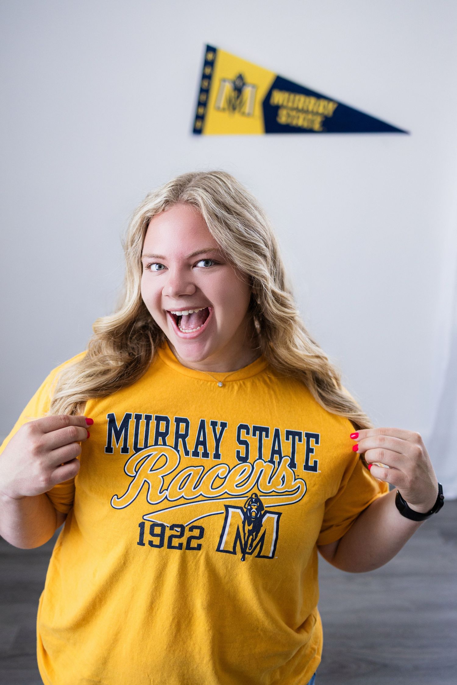 Enthusiastic student showing off Murray State Racers t-shirt with school pennant displayed behind.