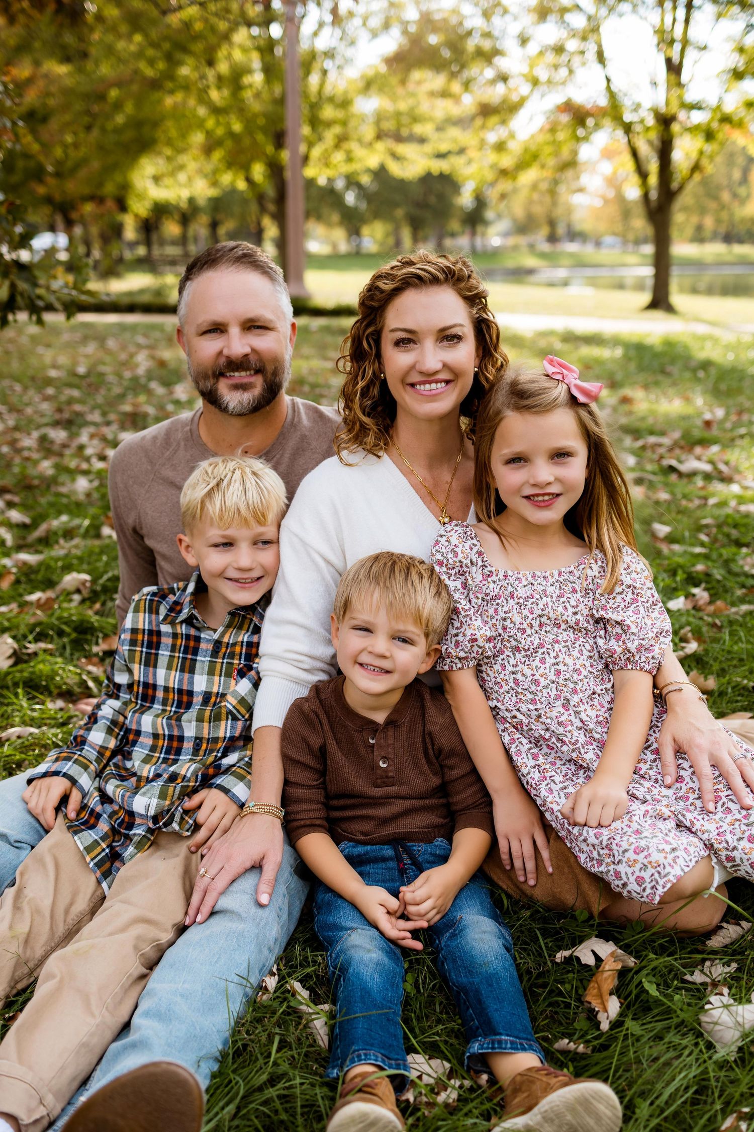 A family sits together on grass during a fall photo session in a park setting.