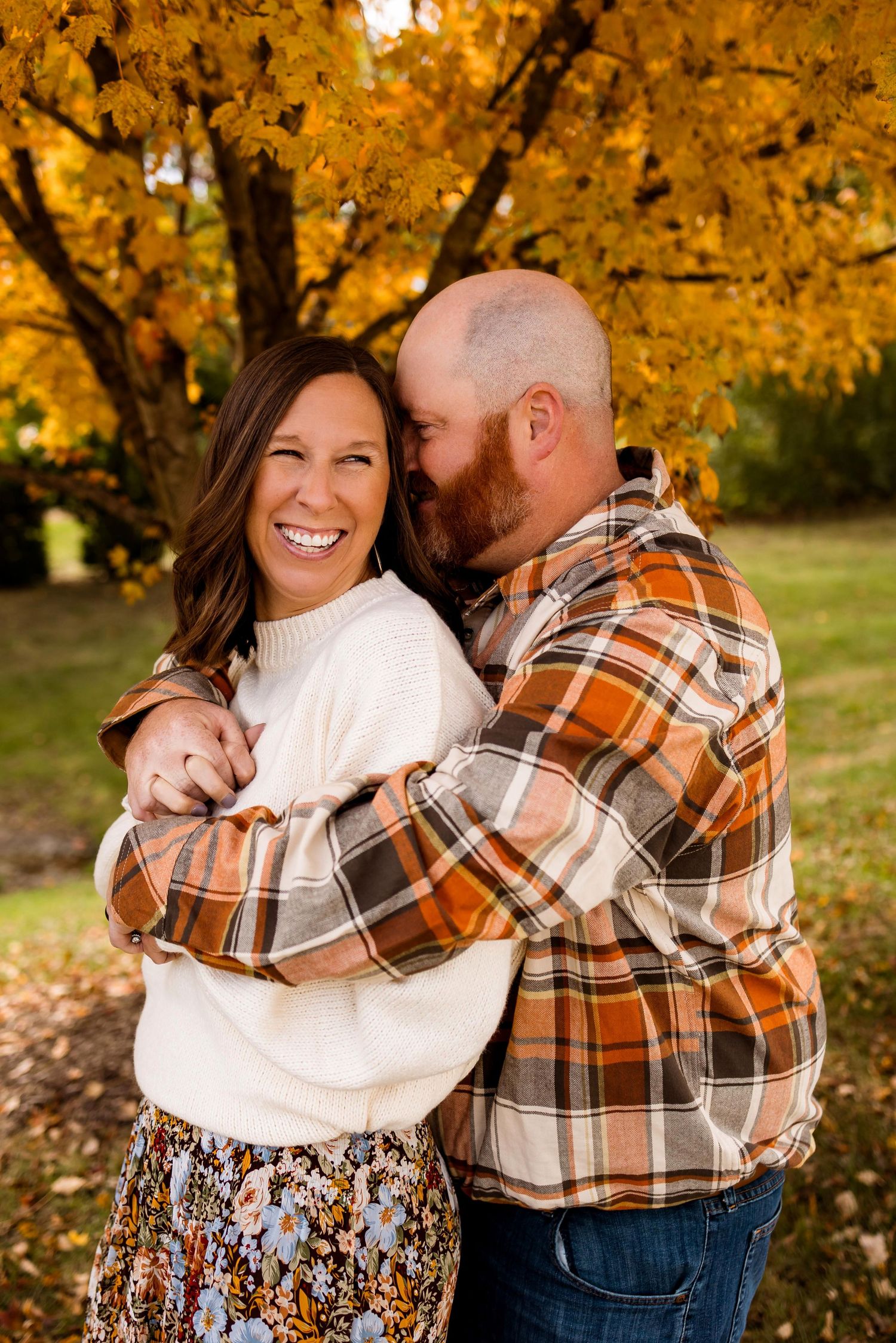 A couple shares intimate moments in a fall setting with golden leaves and warm lighting.