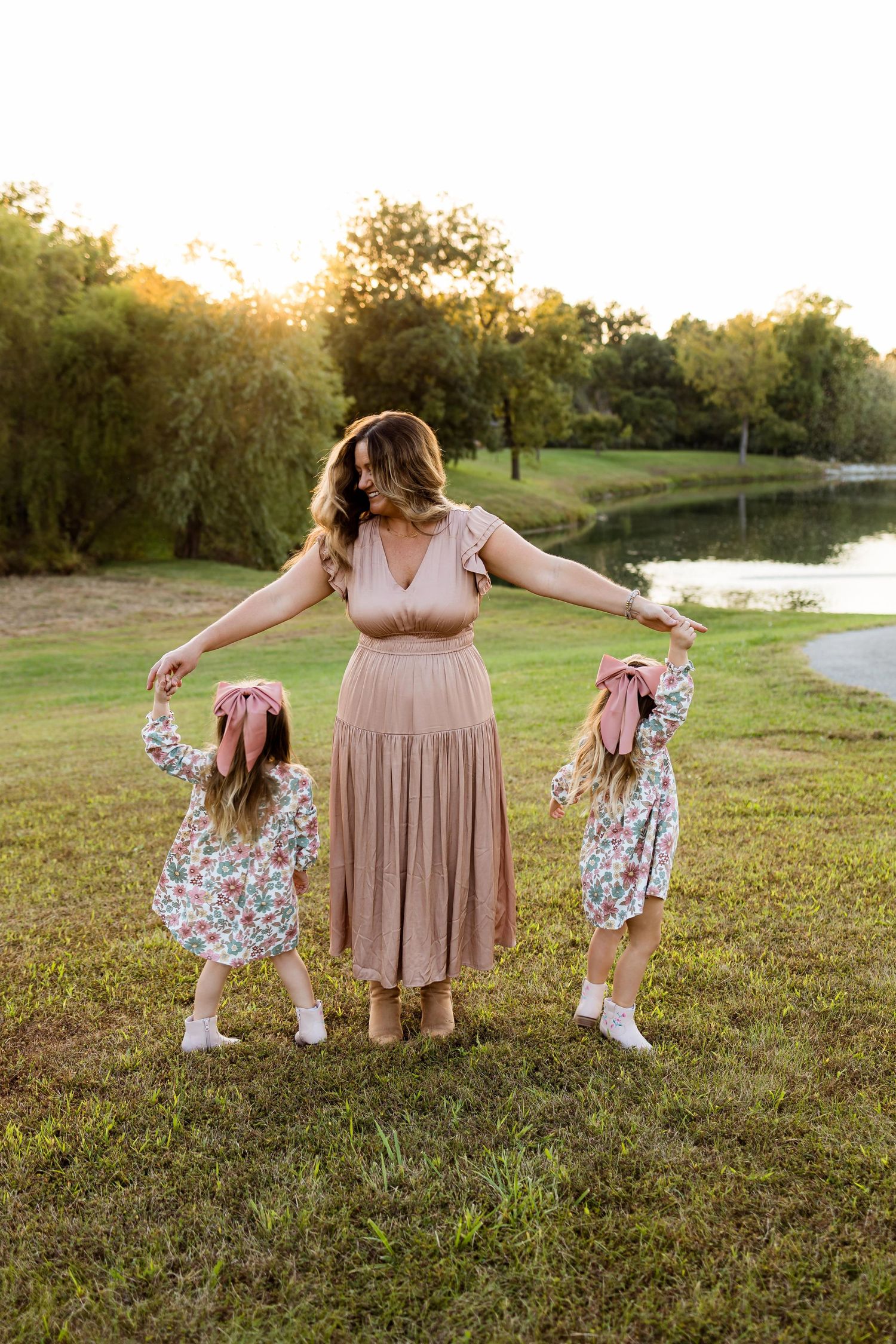 A playful outdoor photoshoot in a grassy field at sunset with coordinated outfits in pink and floral prints.