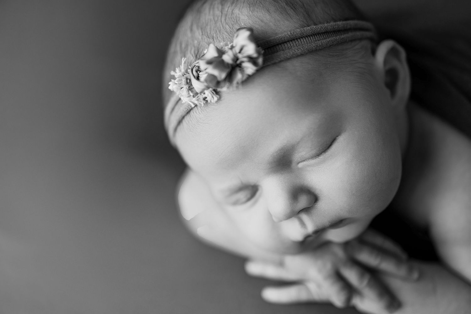 Peaceful sleeping newborn baby in black and white wearing delicate floral headband.