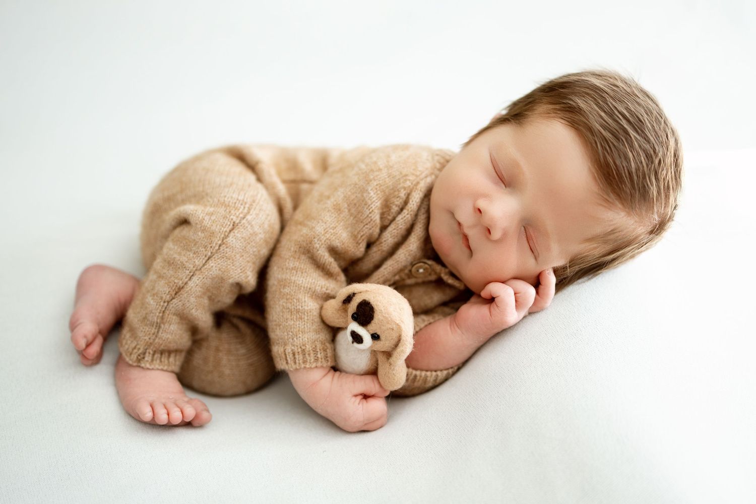 Sleeping newborn baby in brown knit outfit lying on white blanket in four sequential poses.
