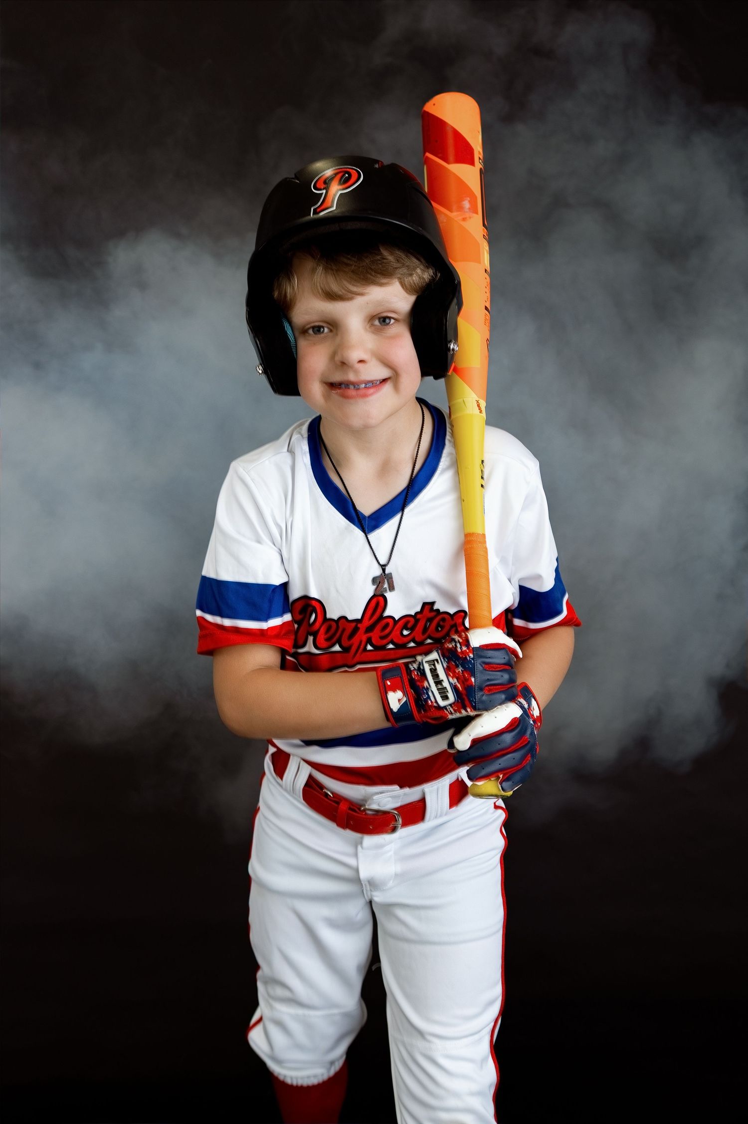 Smiling youth baseball player holding an orange bat during a personality-filled studio sports photography session