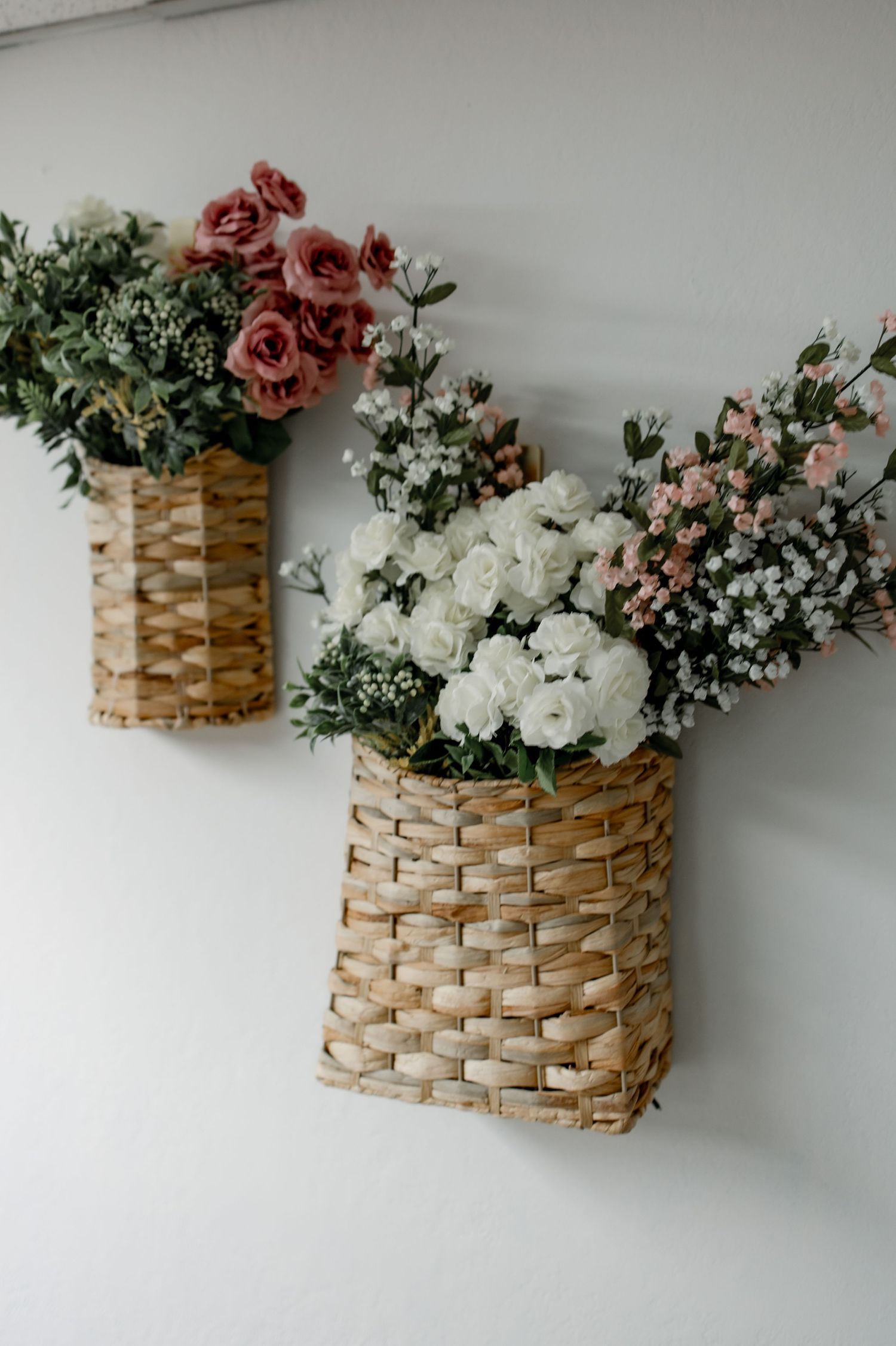 Woven wall basket with pink and white flowers and greenery arranged in a rustic farmhouse style decor.