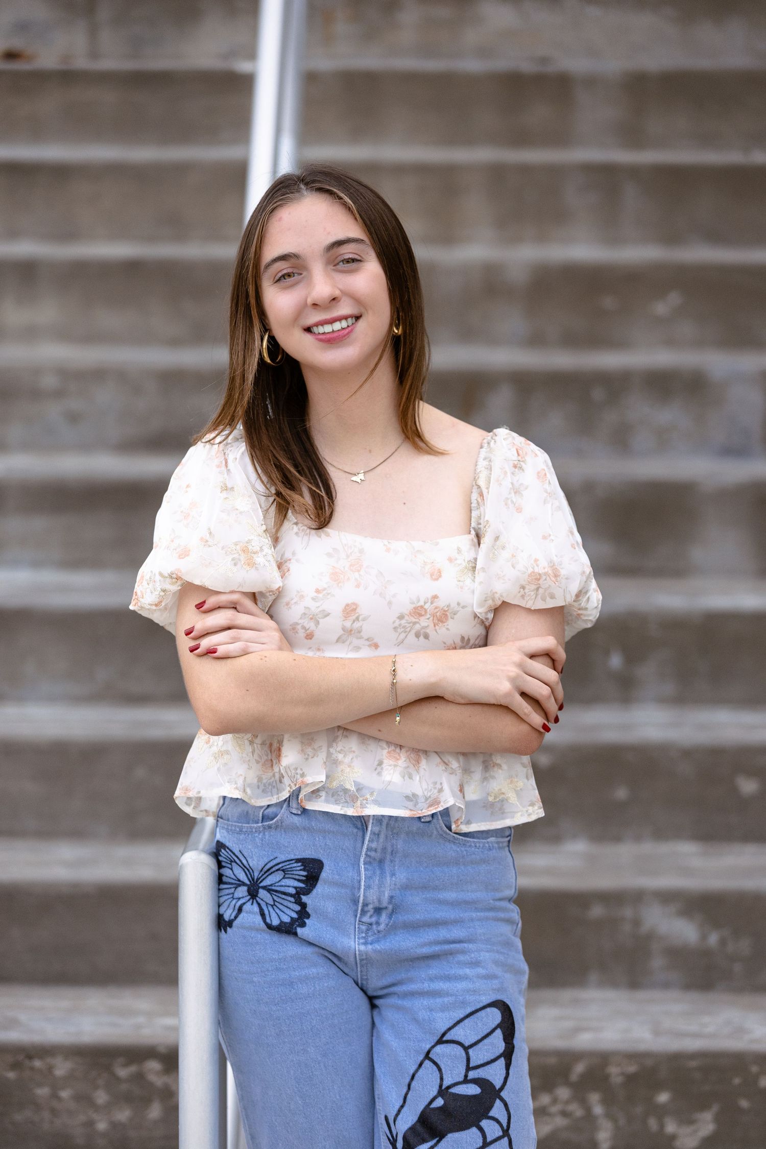 Casual portrait on concrete steps wearing floral top and butterfly-decorated jeans.