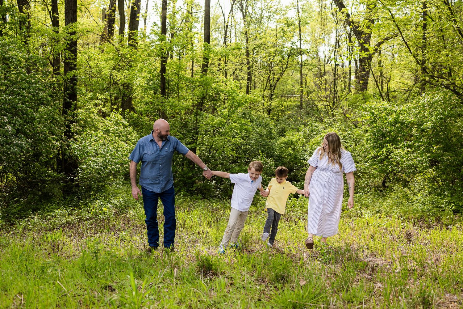 Family holding hands while walking through a vibrant green forest path.