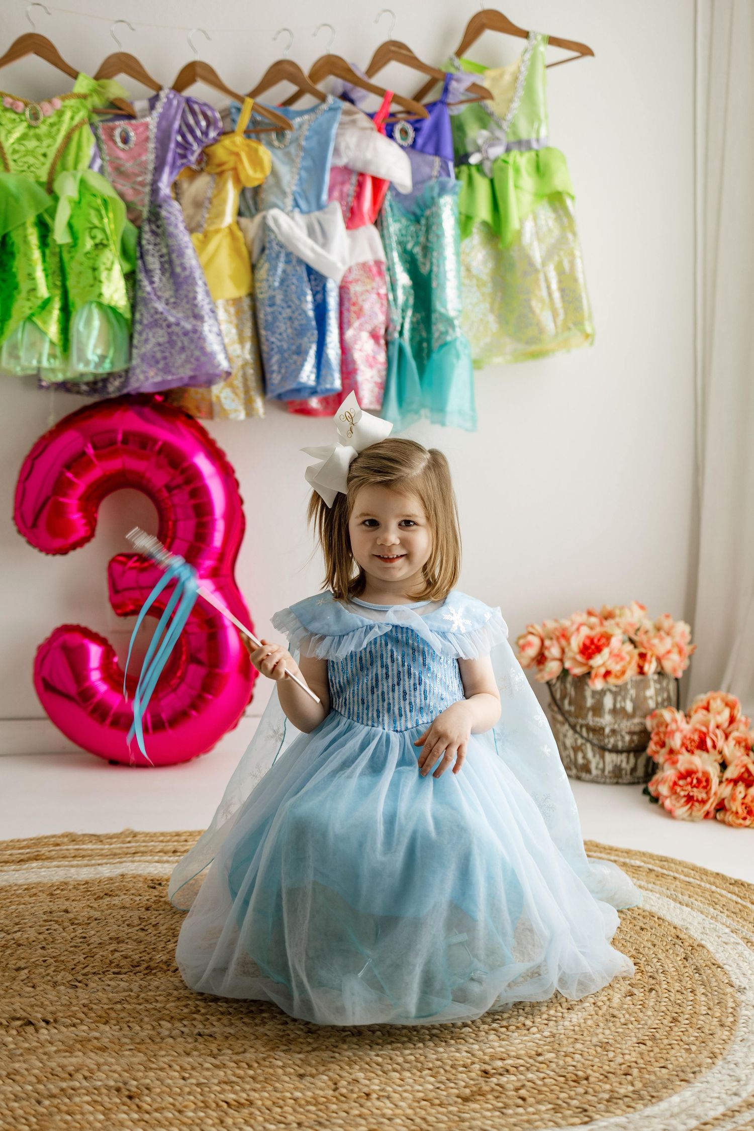 A decorative birthday party setup with pink number balloons and colorful dresses hanging on the wall.
