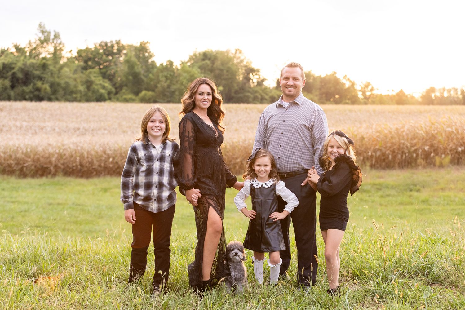 Family of five posing together in field at golden hour.