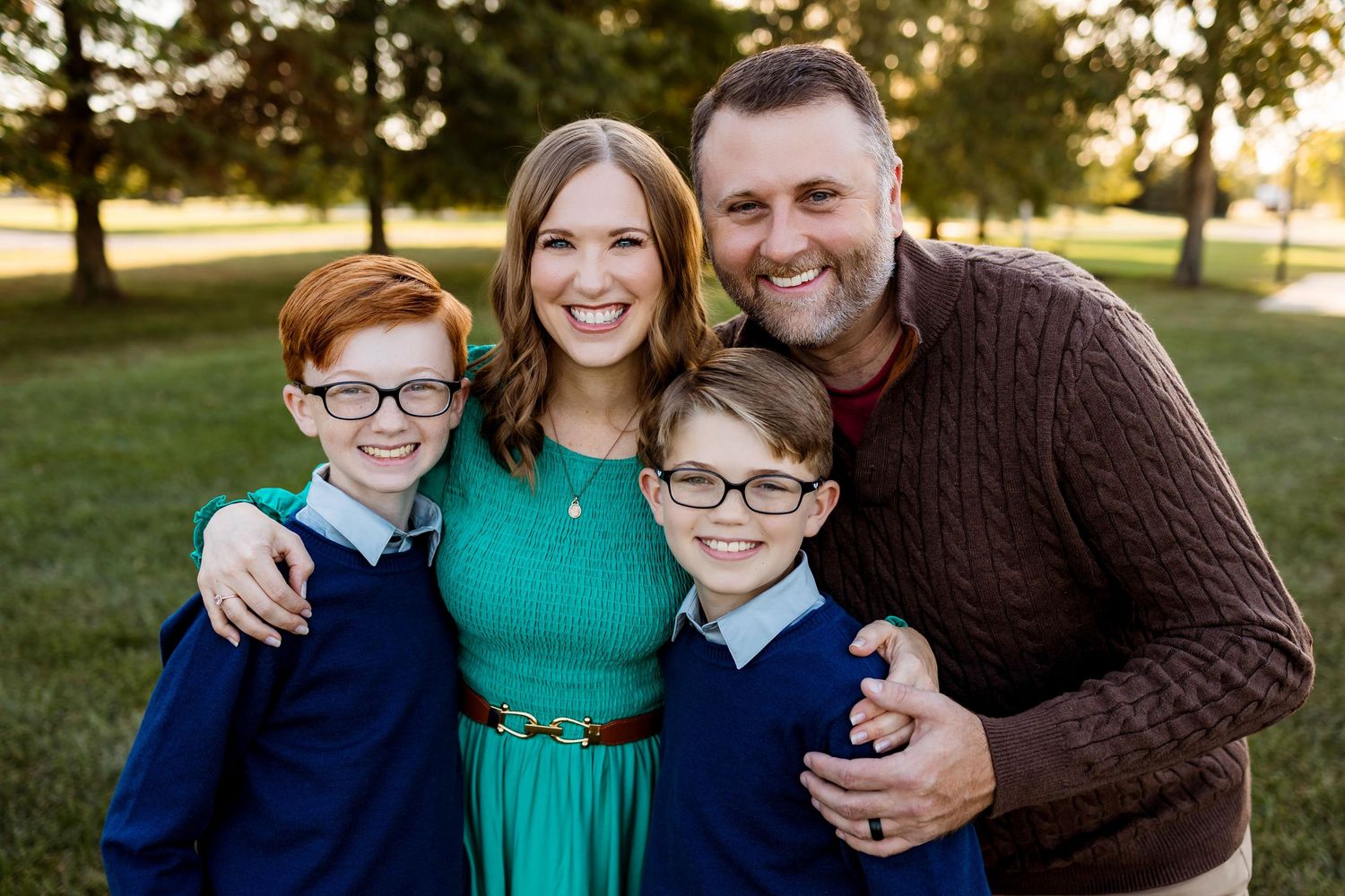 A group poses together outdoors during golden hour for a casual portrait session in a grassy park setting.