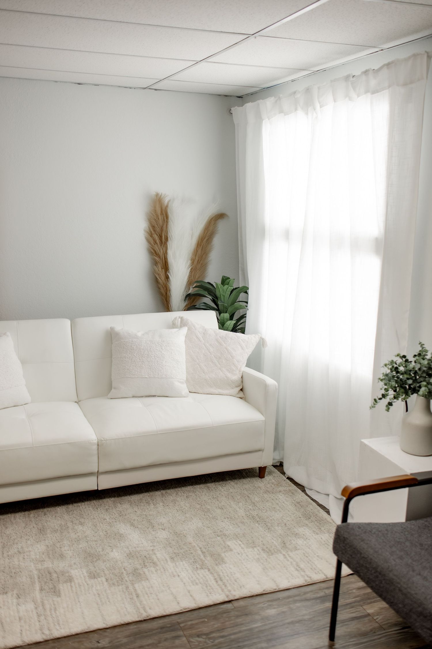 Minimalist photography studio with white couch, natural light, and pampas grass decor against white walls.