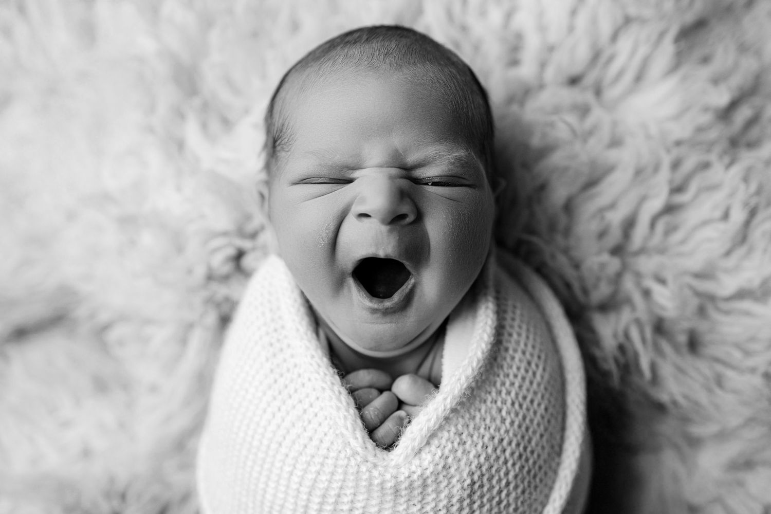 A series of four black and white photos showing a sleeping baby swaddled in white fabric on a soft textured background.