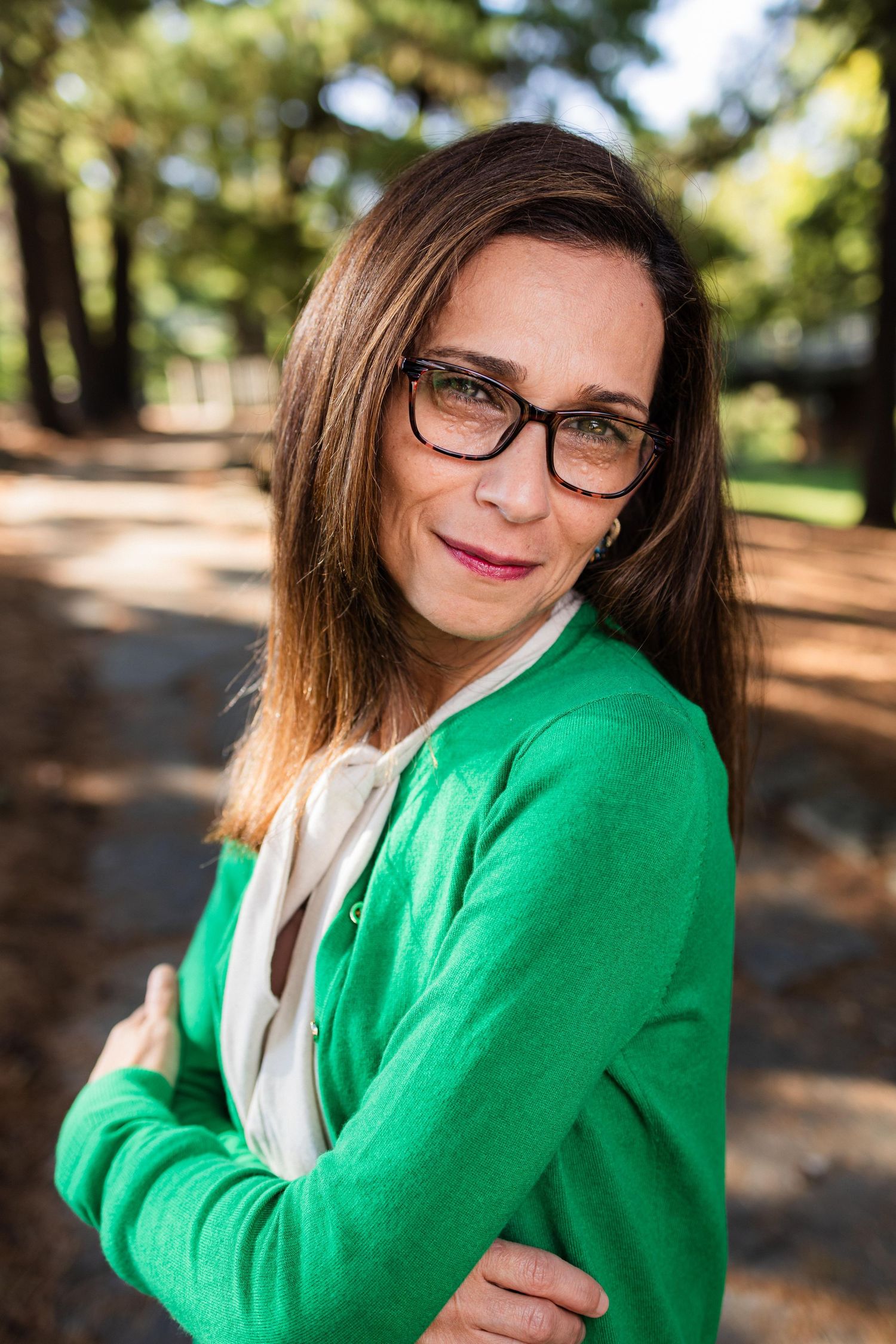 Person in glasses and bright green sweater poses outdoors in a wooded setting with warm natural lighting.