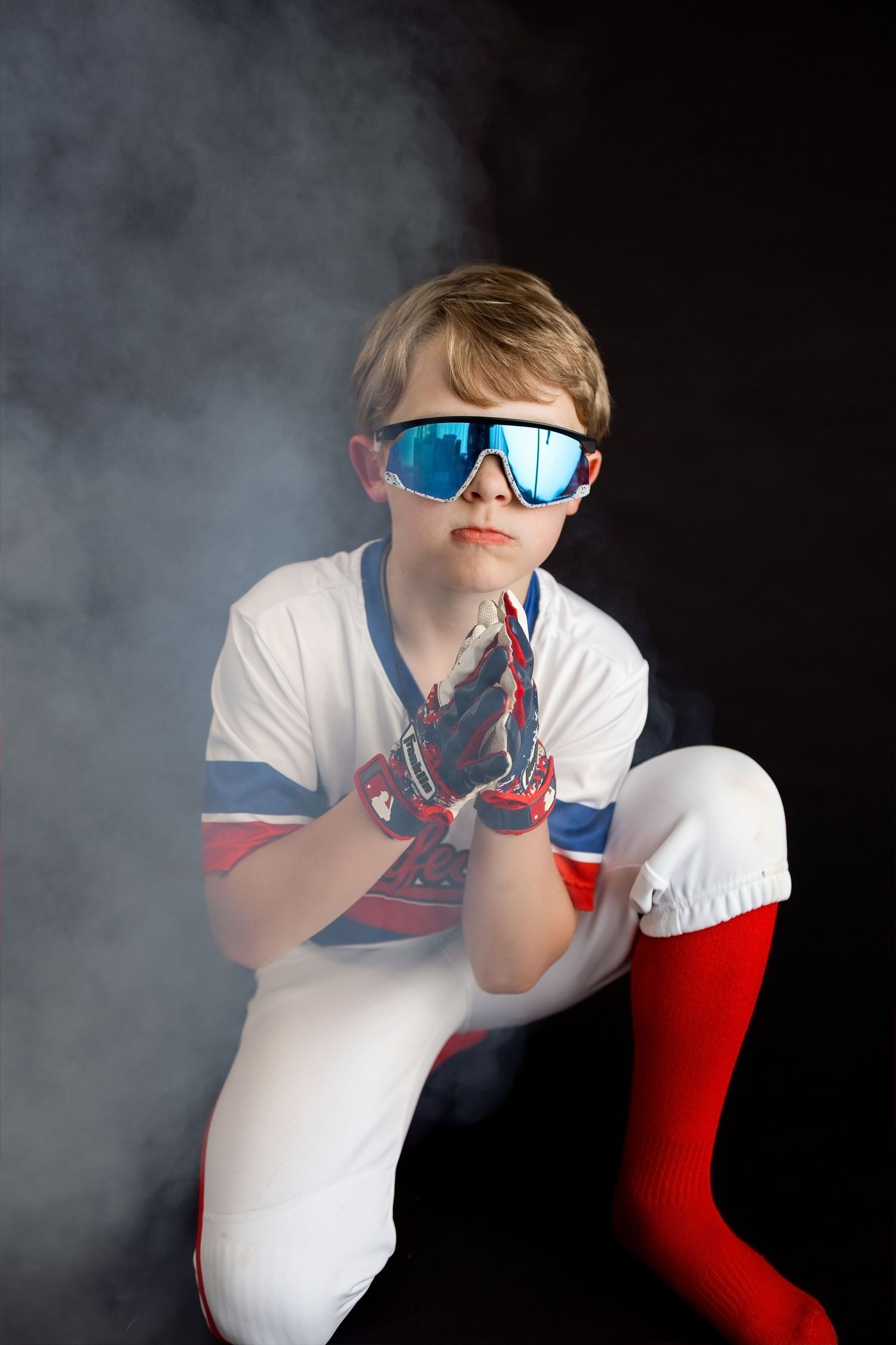 Young baseball player posing with batting gloves and sunglasses during a dramatic sports photography session in Edwardsville