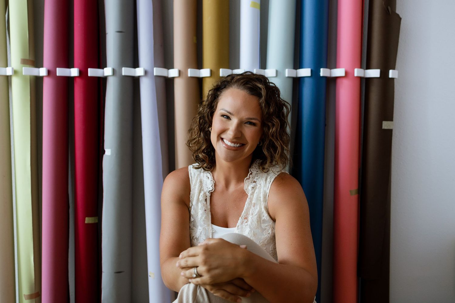 Smiling woman holding fabric swatches standing in front of colorful textile rolls in a fabric store.