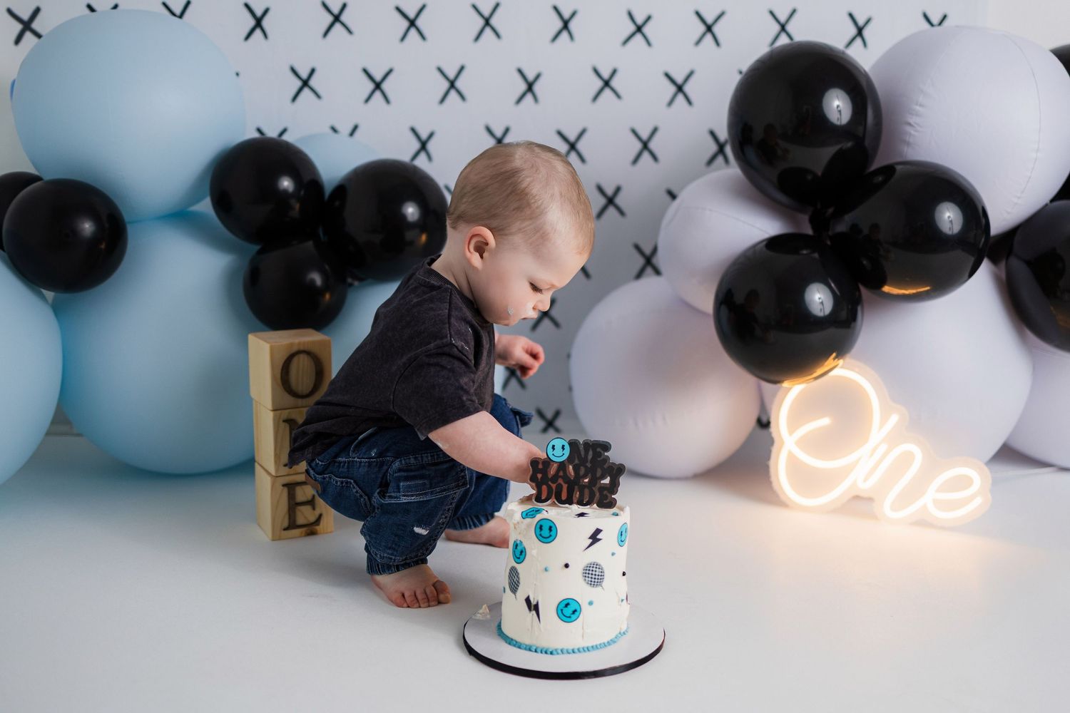 A colorful cake smash photo session setup with black and white balloons and props against a light blue backdrop.
