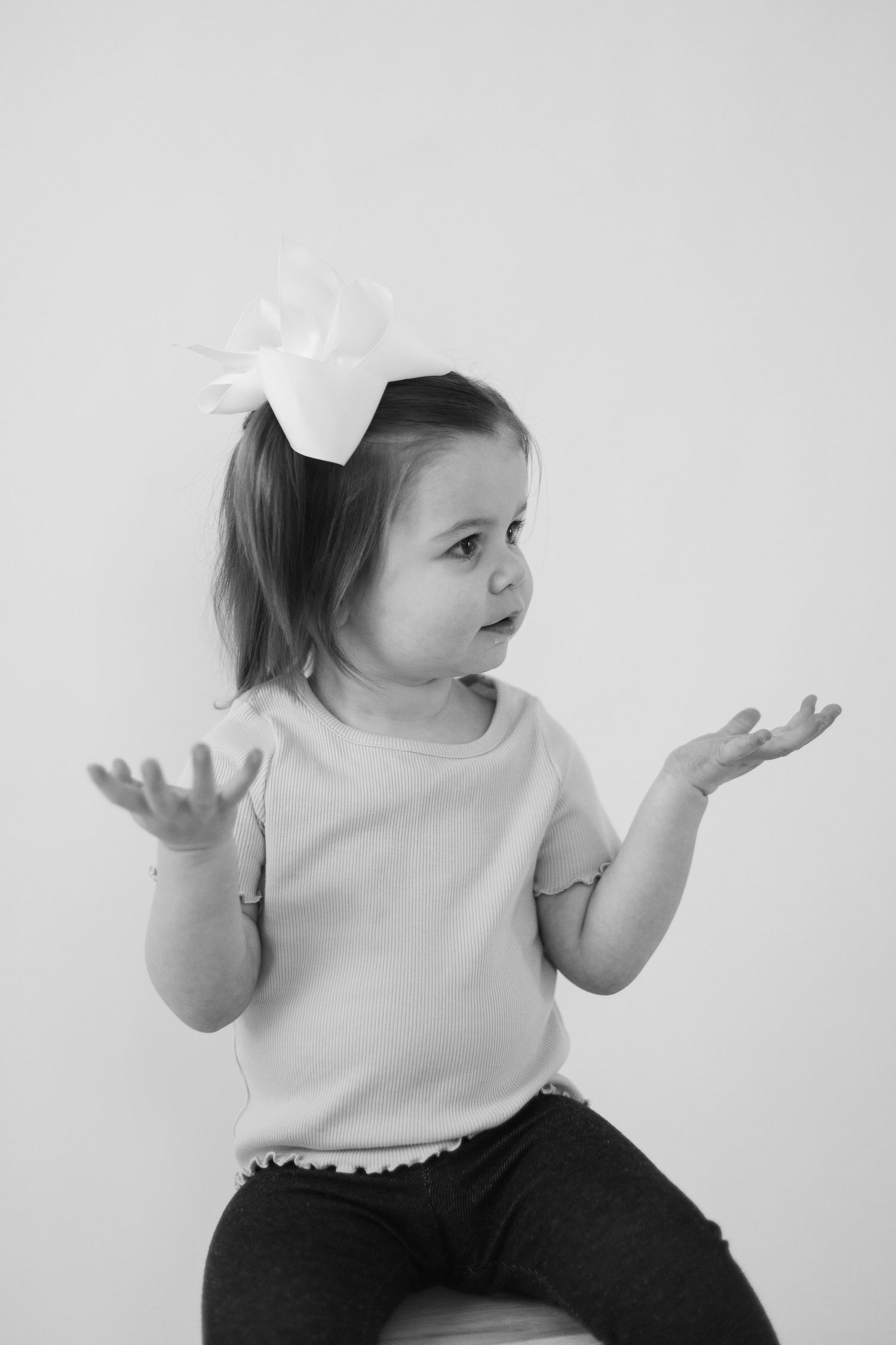 Child in white bow accessory gesturing expressively against light background.