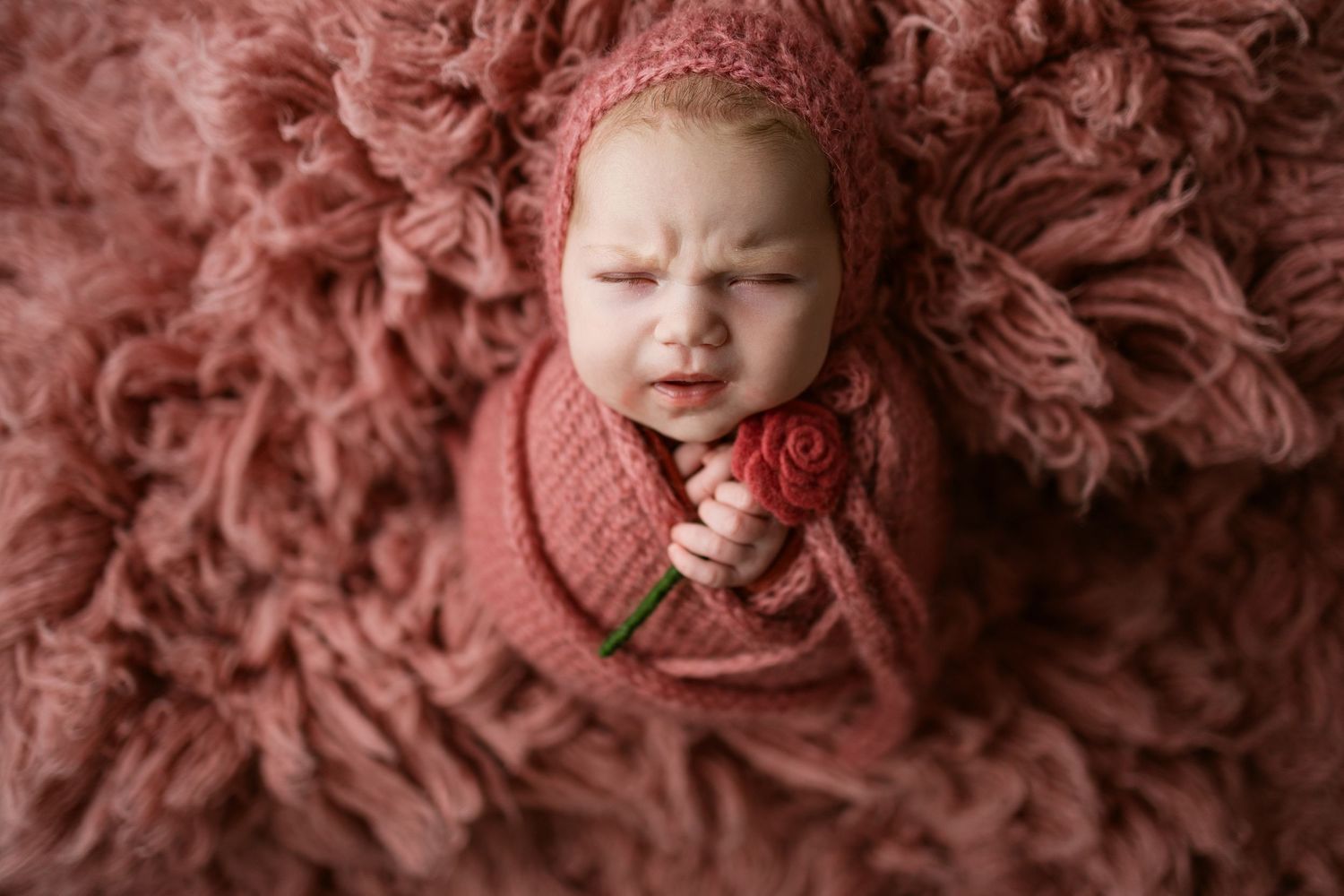 A baby wearing a pink outfit lies on a soft pink textured blanket while sleeping peacefully.