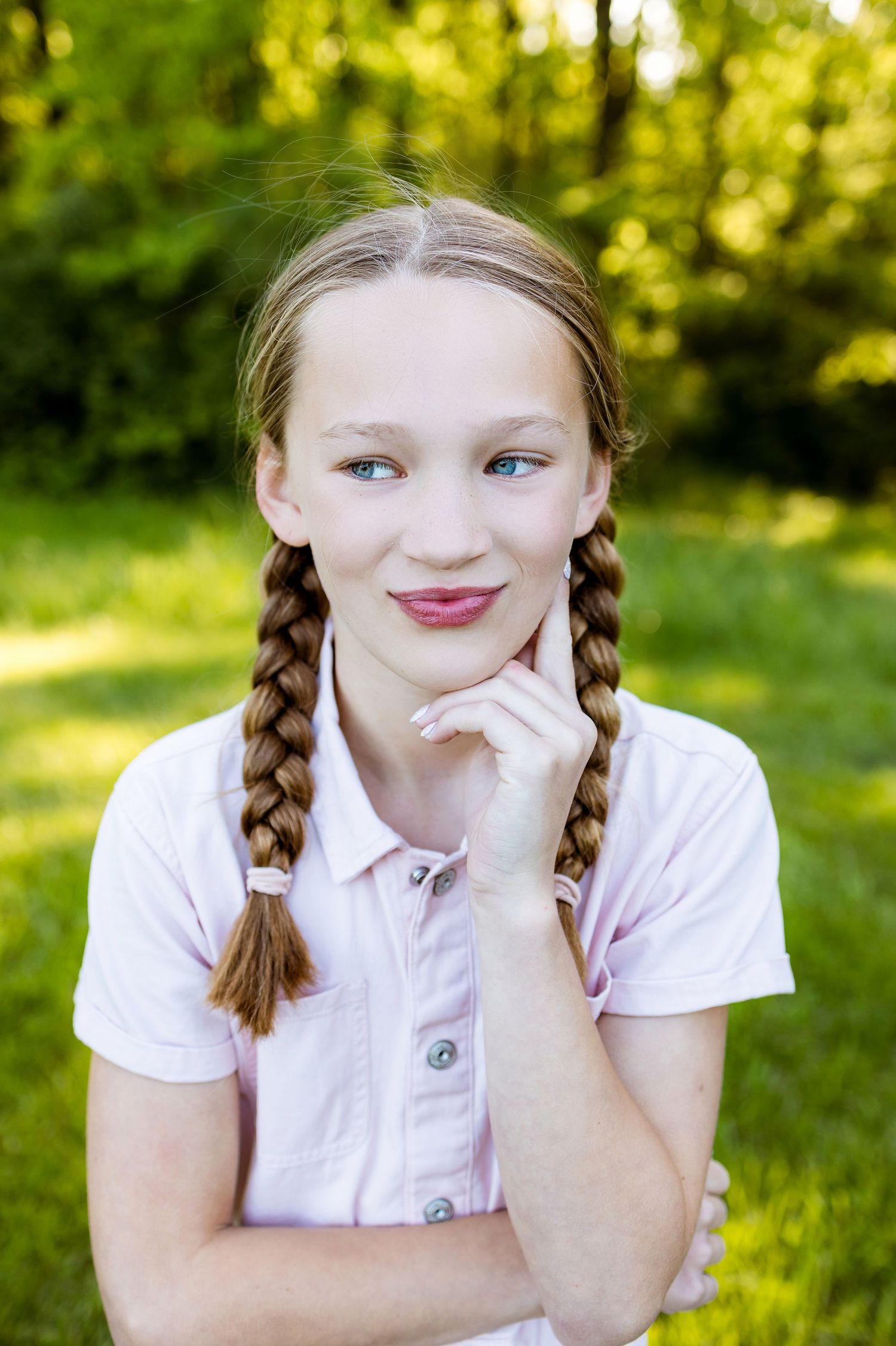 Young person with braided hair poses thoughtfully in white shirt against sunny natural background.