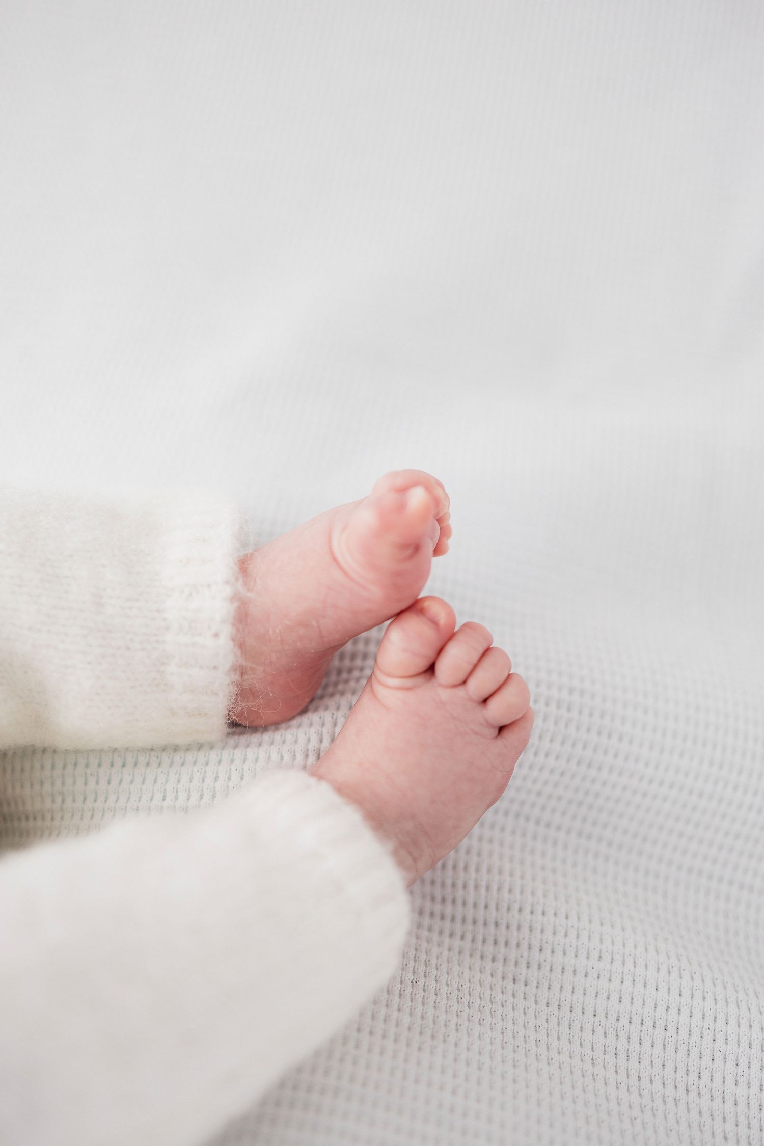 Close-up of tiny pink newborn baby feet on white textured blanket.