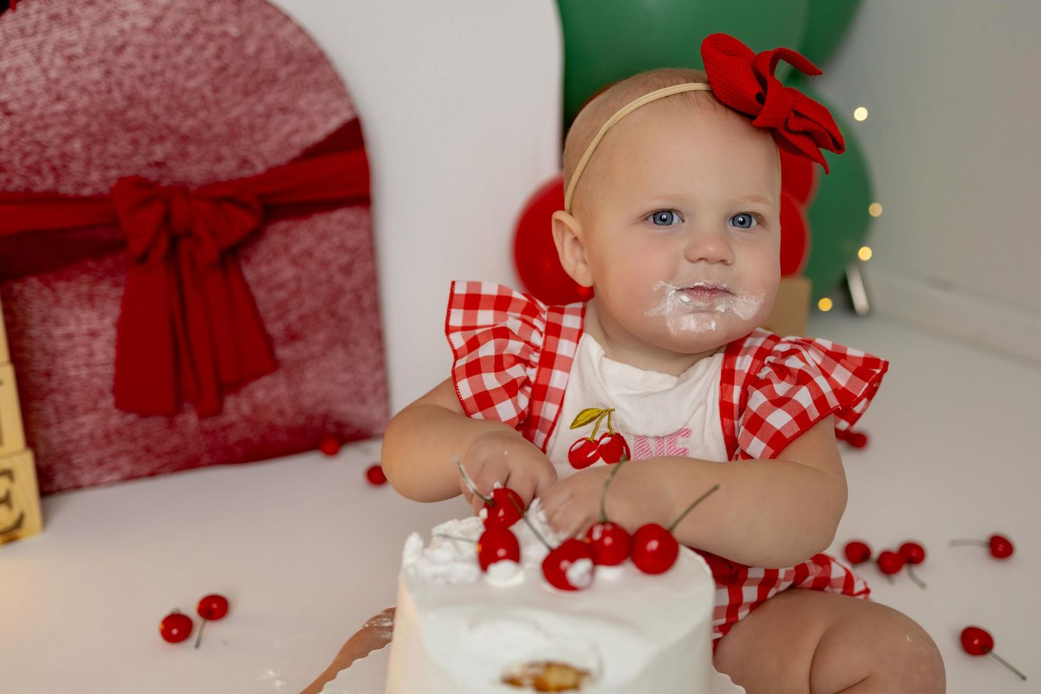 Red and green party decor with cherries and gingham patterns create a festive first birthday scene.