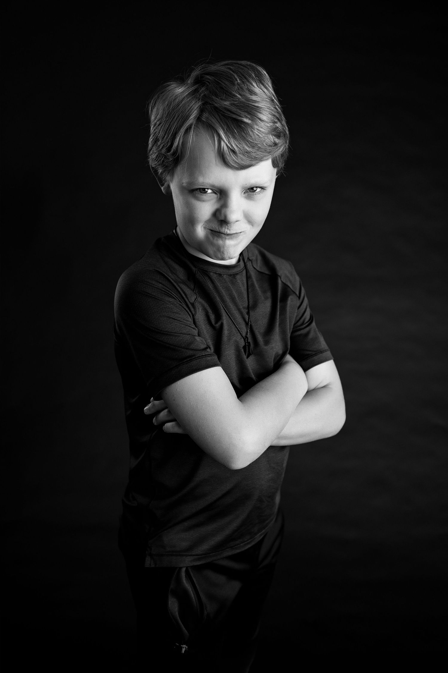 Black-and-white personality portrait of a young boy smirking with his arms crossed at the TLP studio