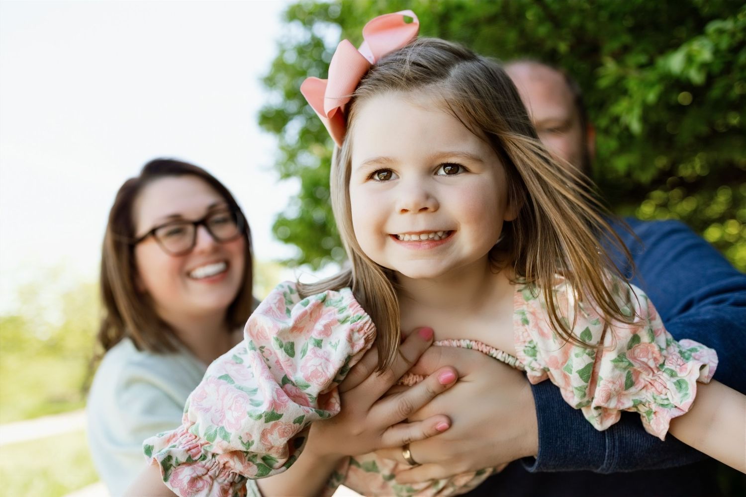 Parents sharing a playful moment with their smiling daughter during an outdoor family photography session