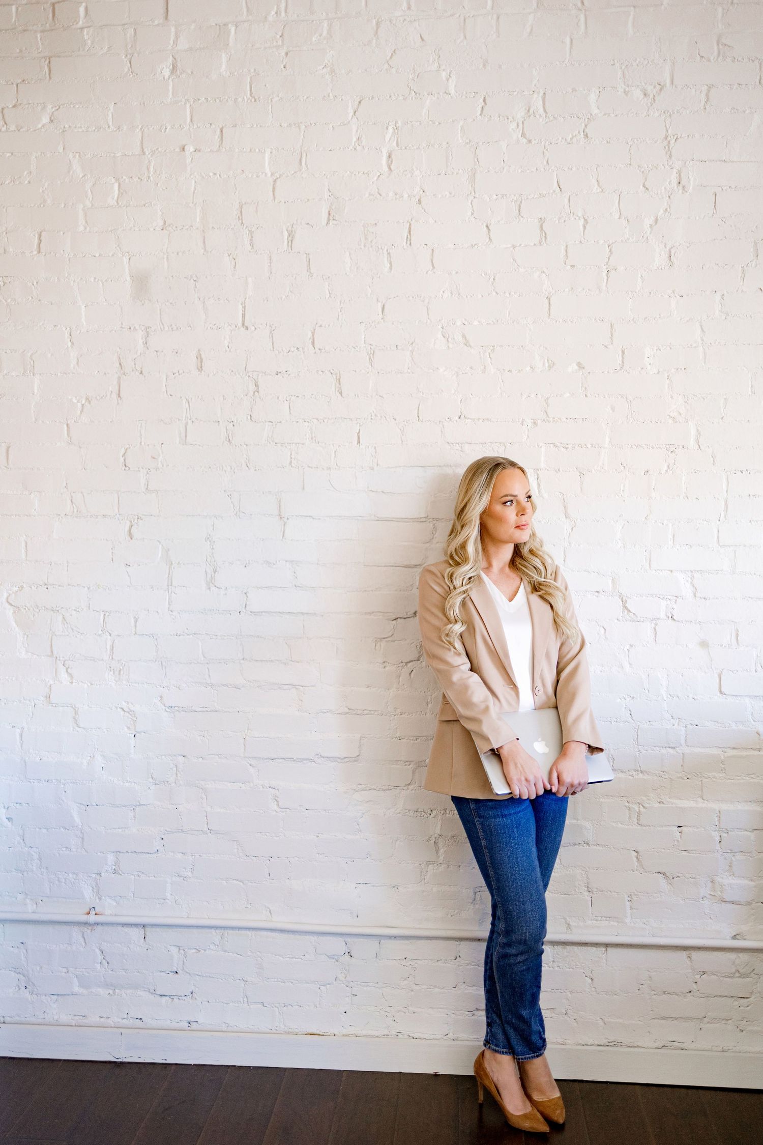 Professional fashion photoshoot against white brick wall showing casual business style outfit with jeans and blazer.