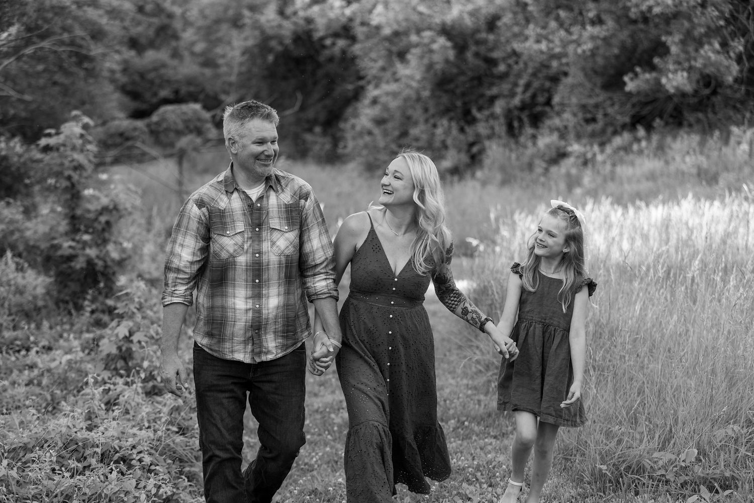 Family walking together through tall grass in black and white photograph.