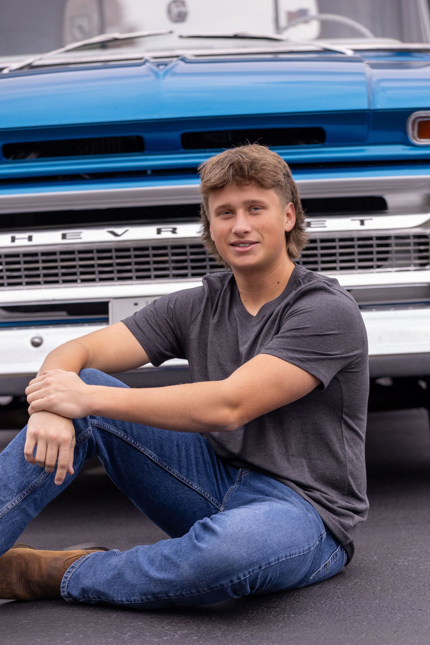 Casual portrait of person sitting against classic blue Chevrolet truck grille.
