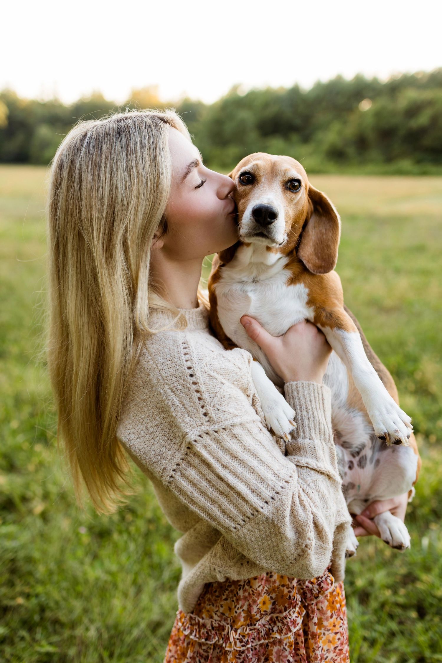 Woman in cream sweater and floral skirt shares sweet moments with beagle puppy in outdoor field setting.