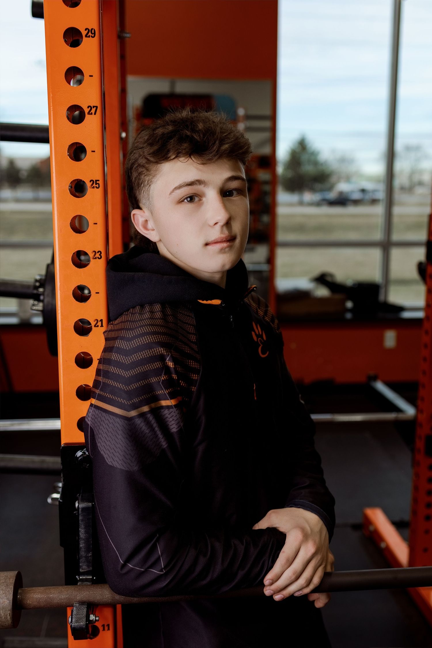 Person in dark clothing sits thoughtfully at a fitness equipment station with orange metal frame visible in background.