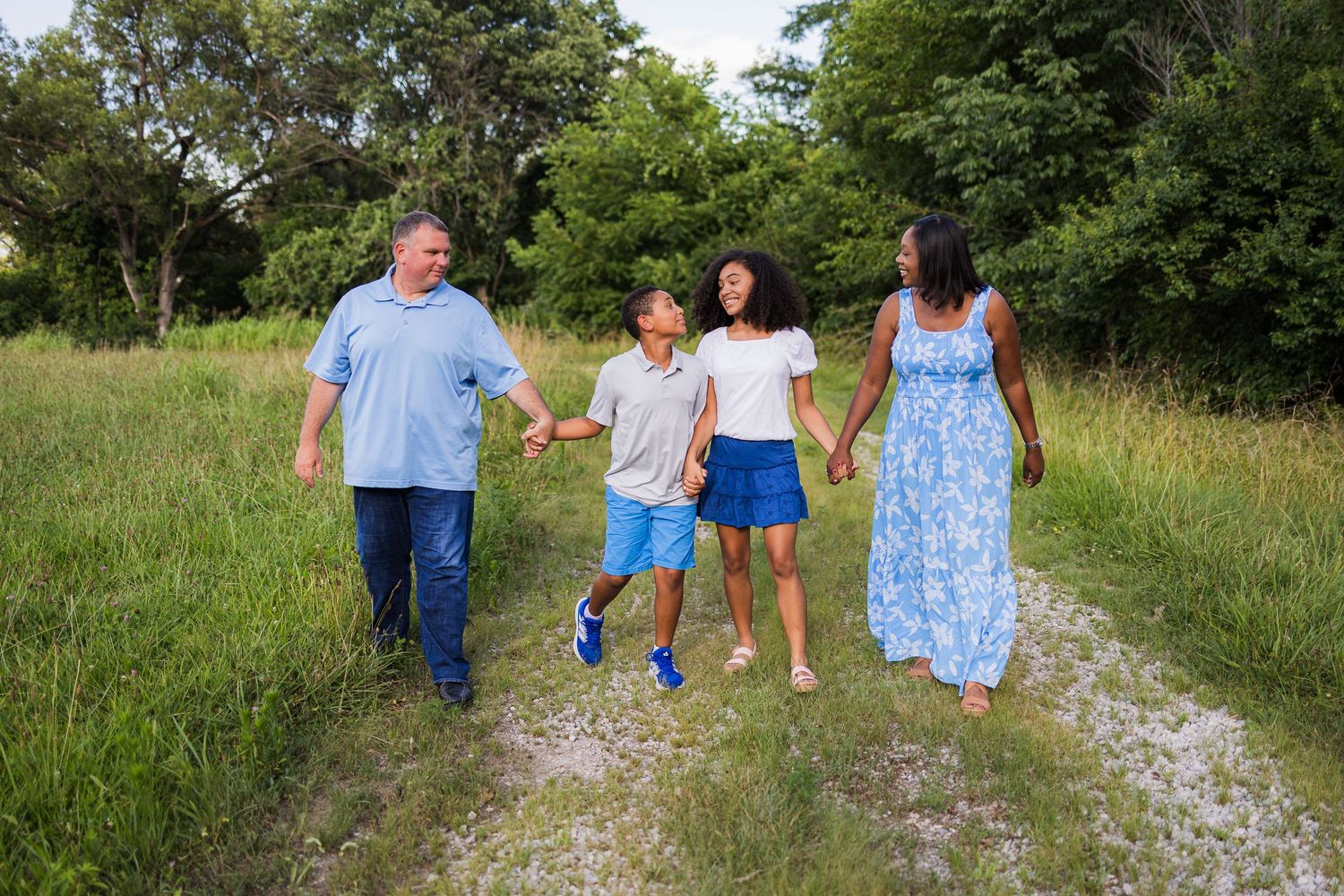 A group walks together on a grassy path through green fields on a sunny summer day.