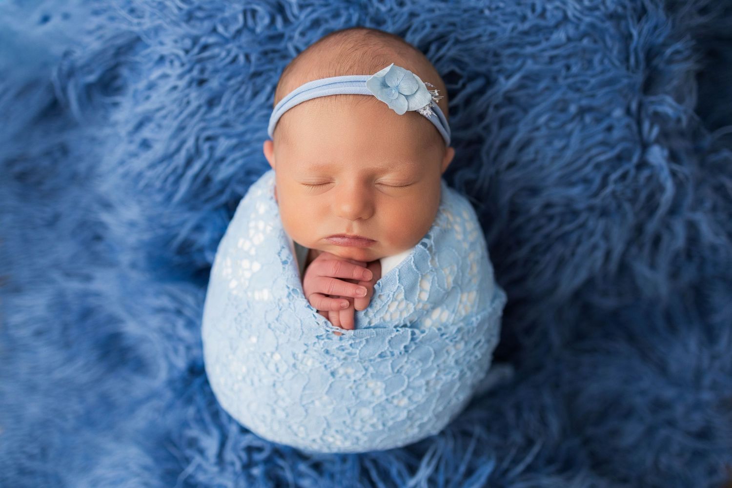 Newborn photography series with baby wrapped in soft blue blankets against navy textured backdrop.
