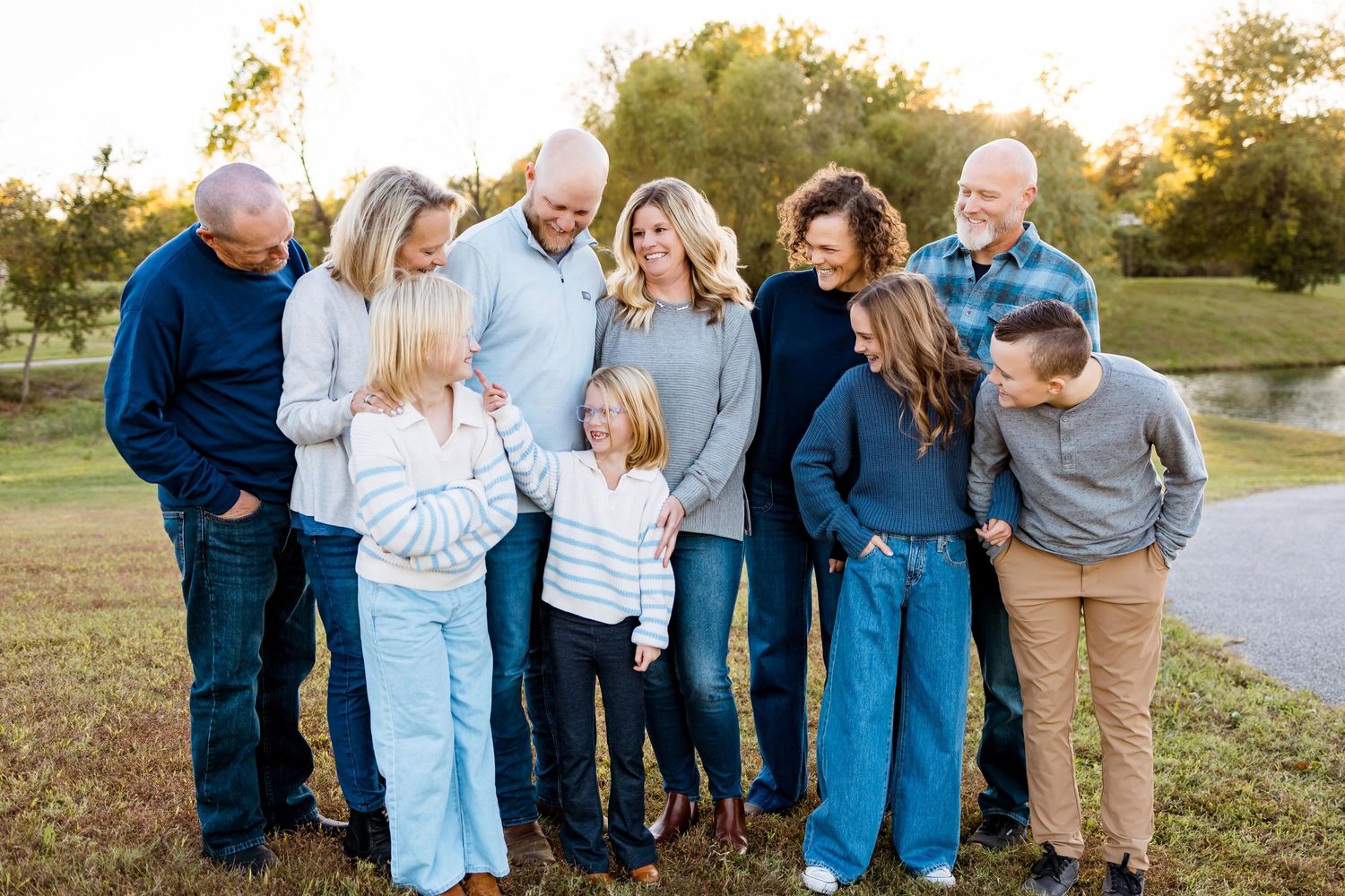Family members wearing coordinating blue and white outfits pose together during golden hour in a park setting.