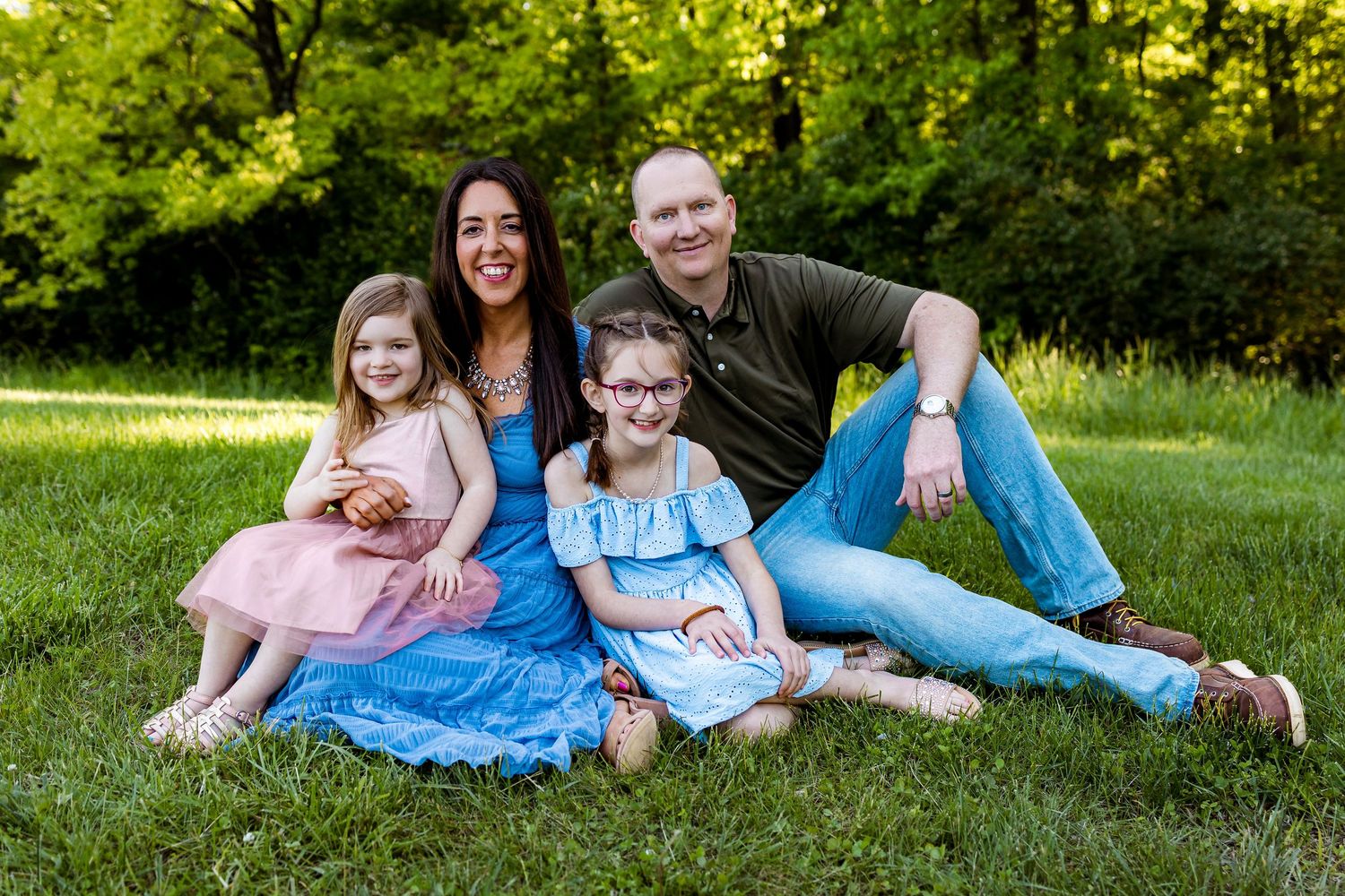 Happy family of four relaxing together on green grass during outdoor summer photoshoot.