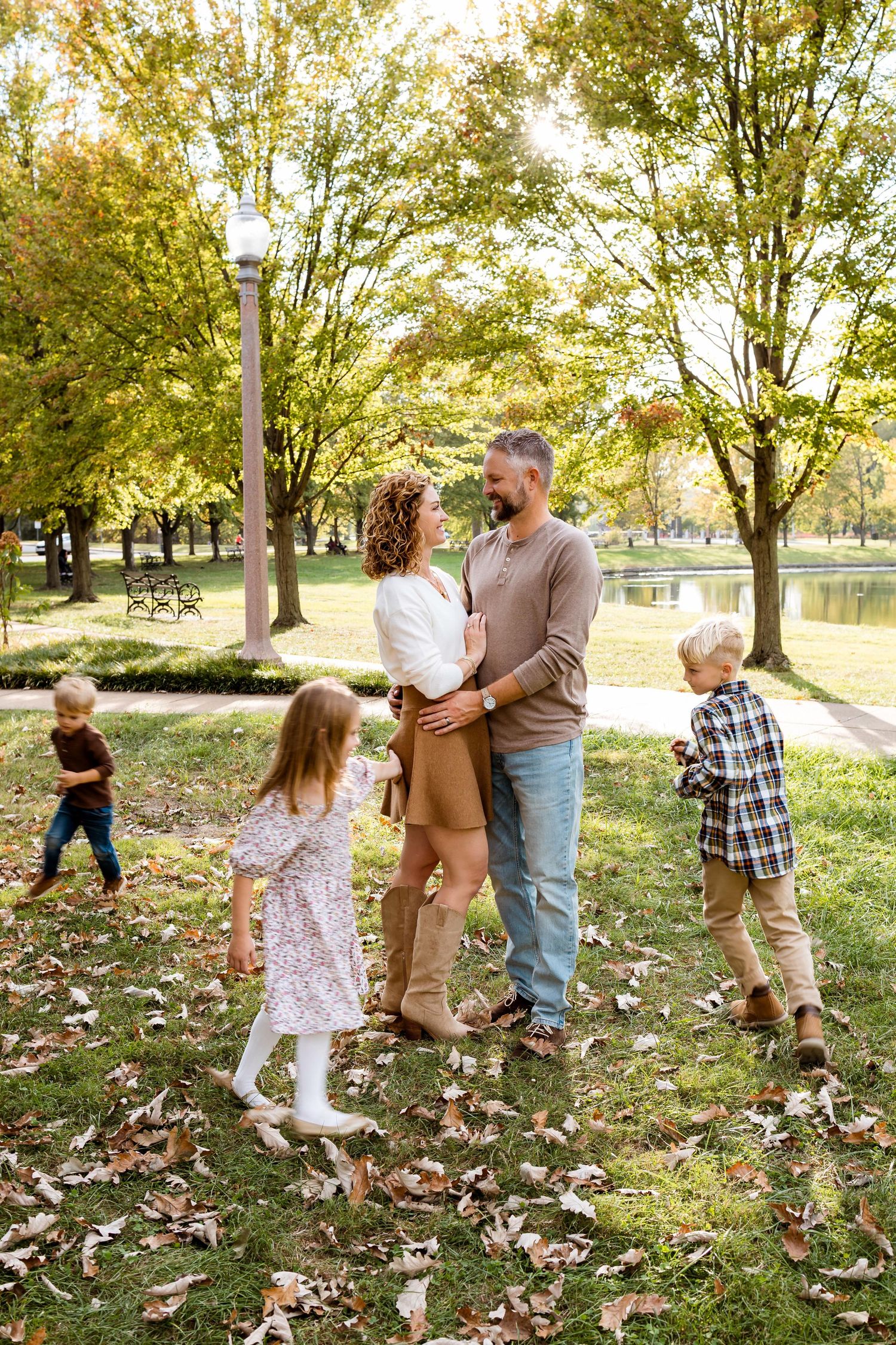 A family plays together in a park on an autumn day with fallen leaves scattered across the grass.
