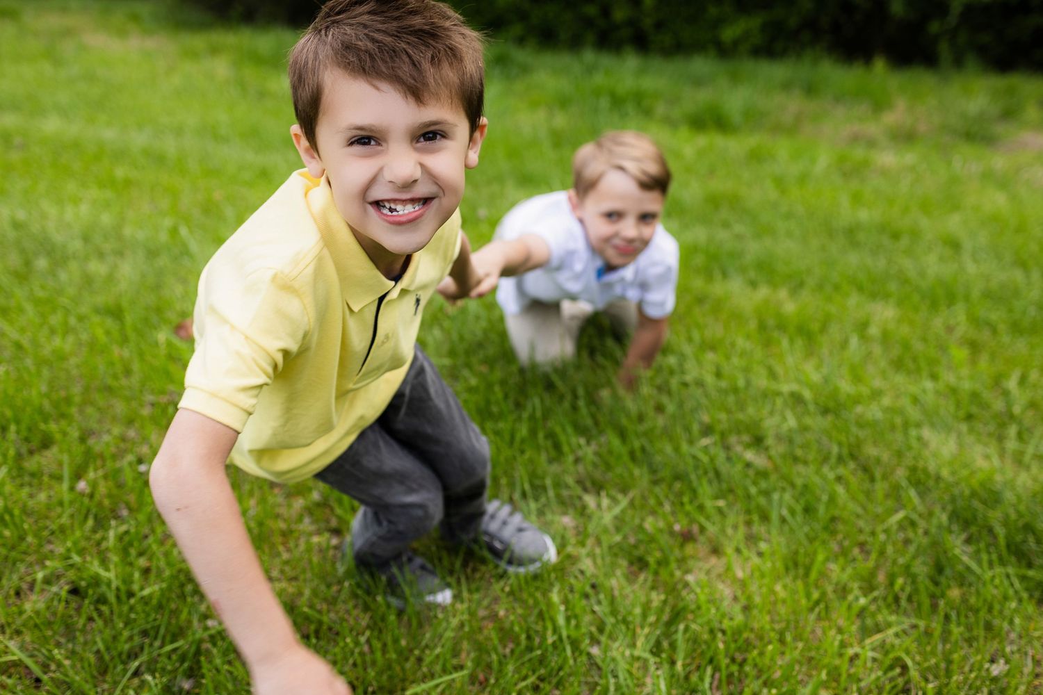 Two children playing and crouching on green grass.