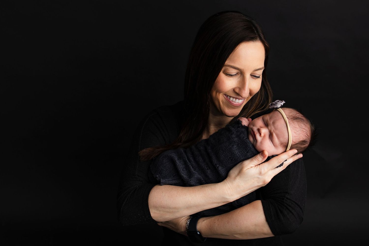 Dramatic studio portrait against black background showing tender maternal moment.