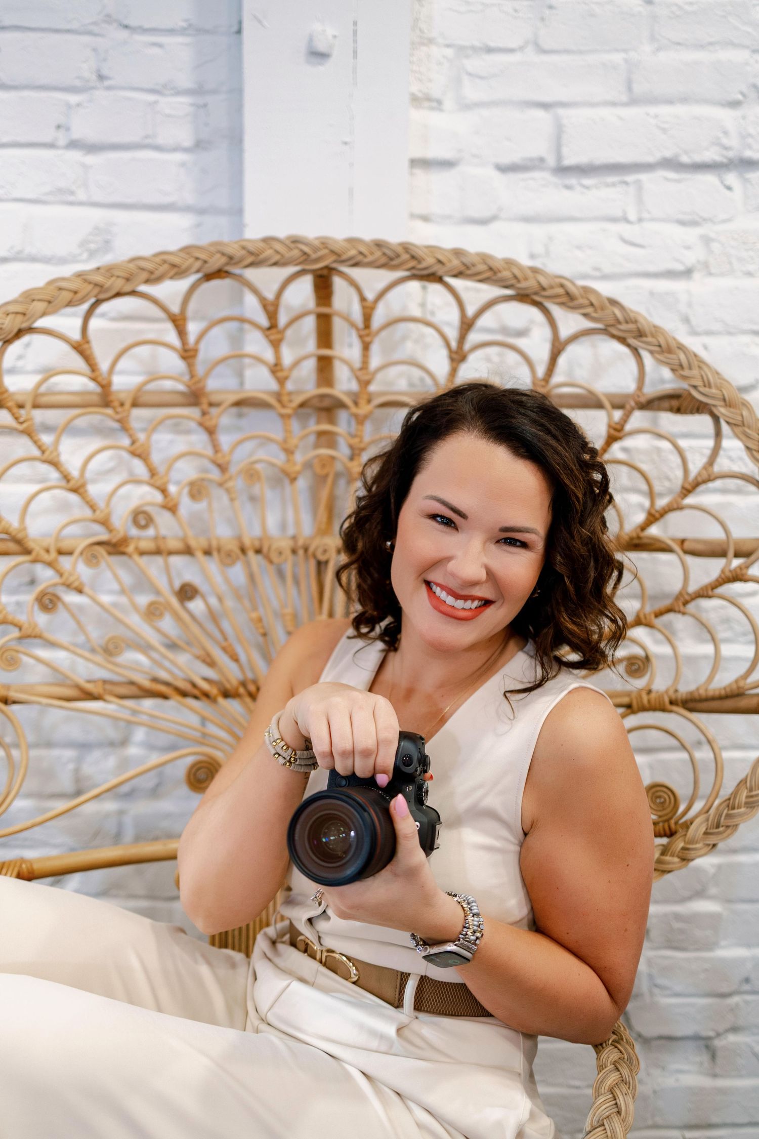 Artistic portrait session featuring wicker peacock chair and camera against white brick wall.