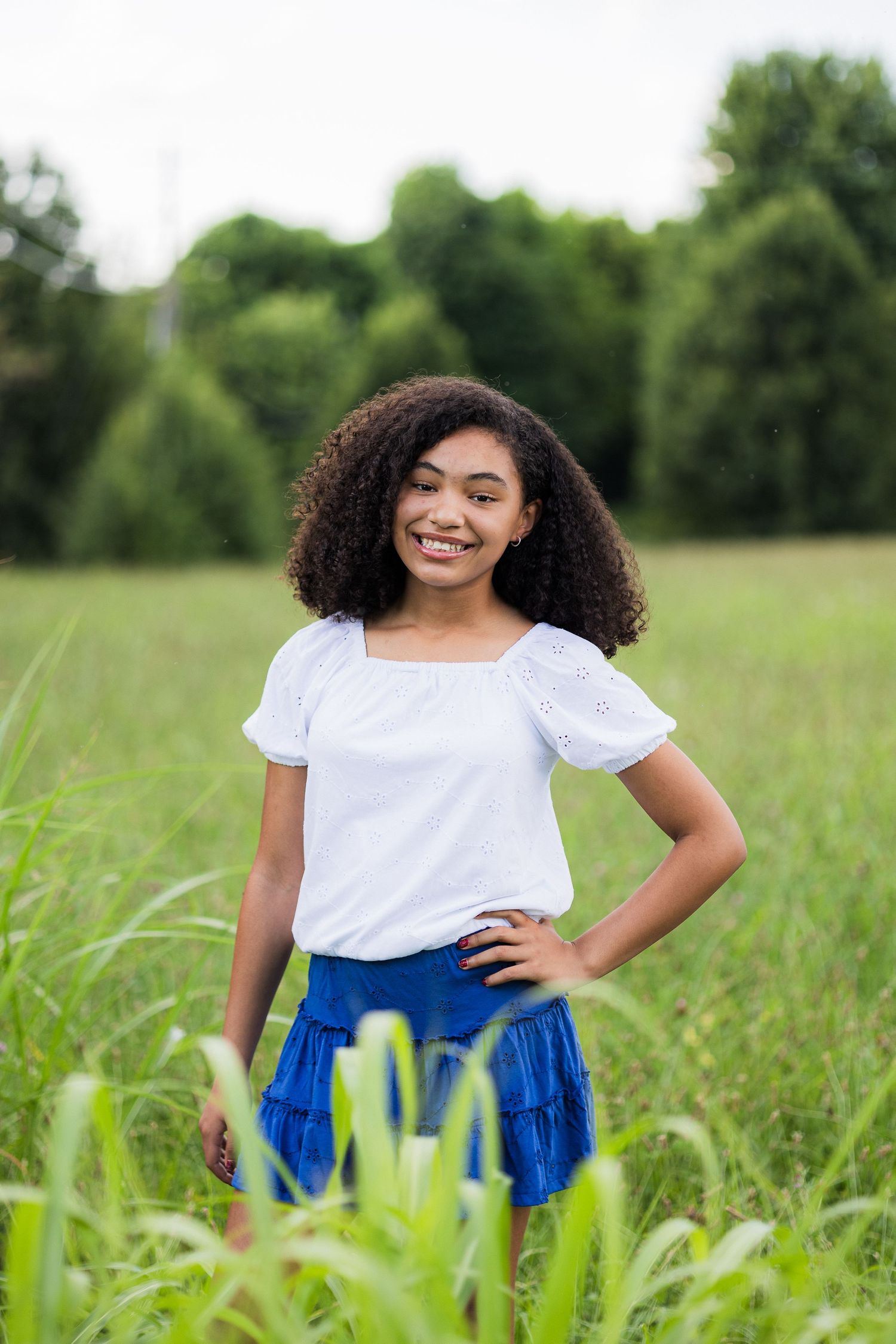 A vibrant outdoor portrait in a grassy field features a flowing white top paired with bright blue clothing.