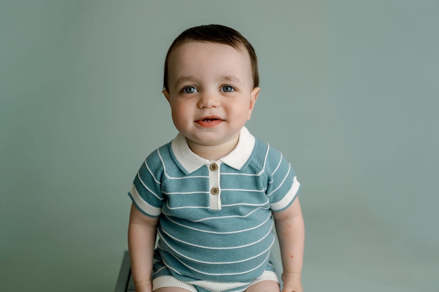 Smiling baby photographed against a sage green backdrop during a first-birthday milestone session at TLP