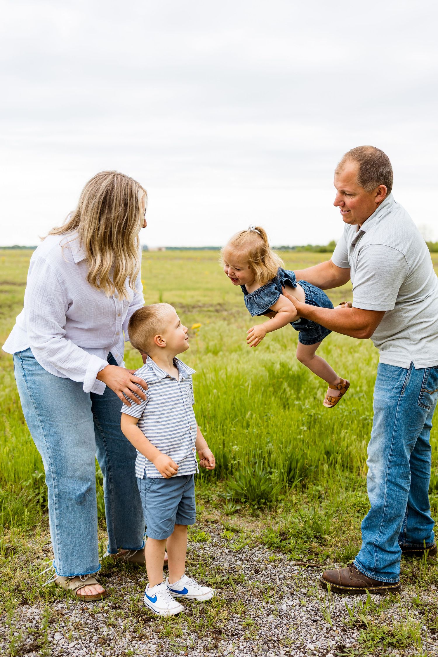 Parents playing and lifting child in the air while another child watches on a summer day.