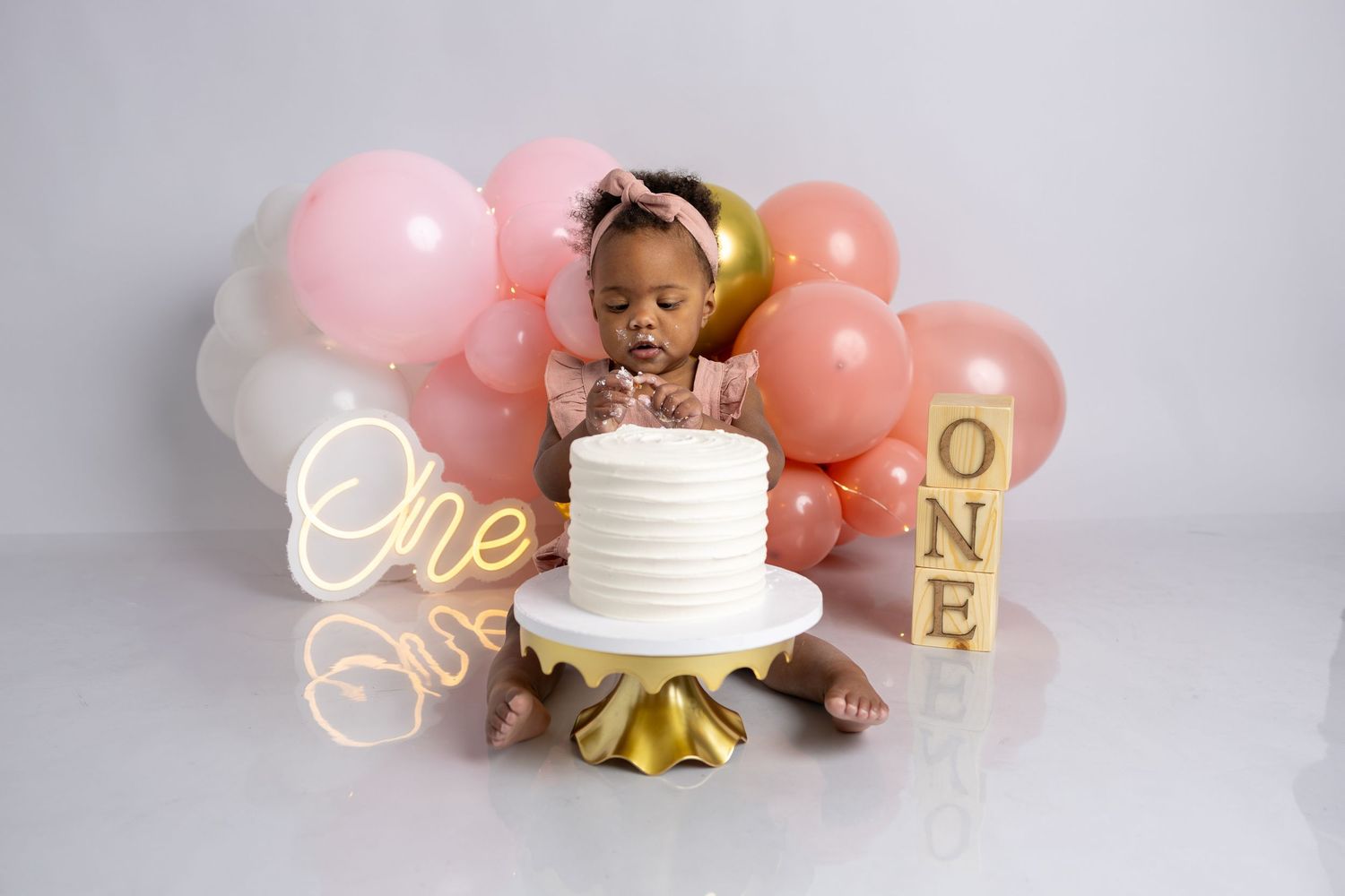 First birthday setup with pink balloons, white cake, and gold decorations.